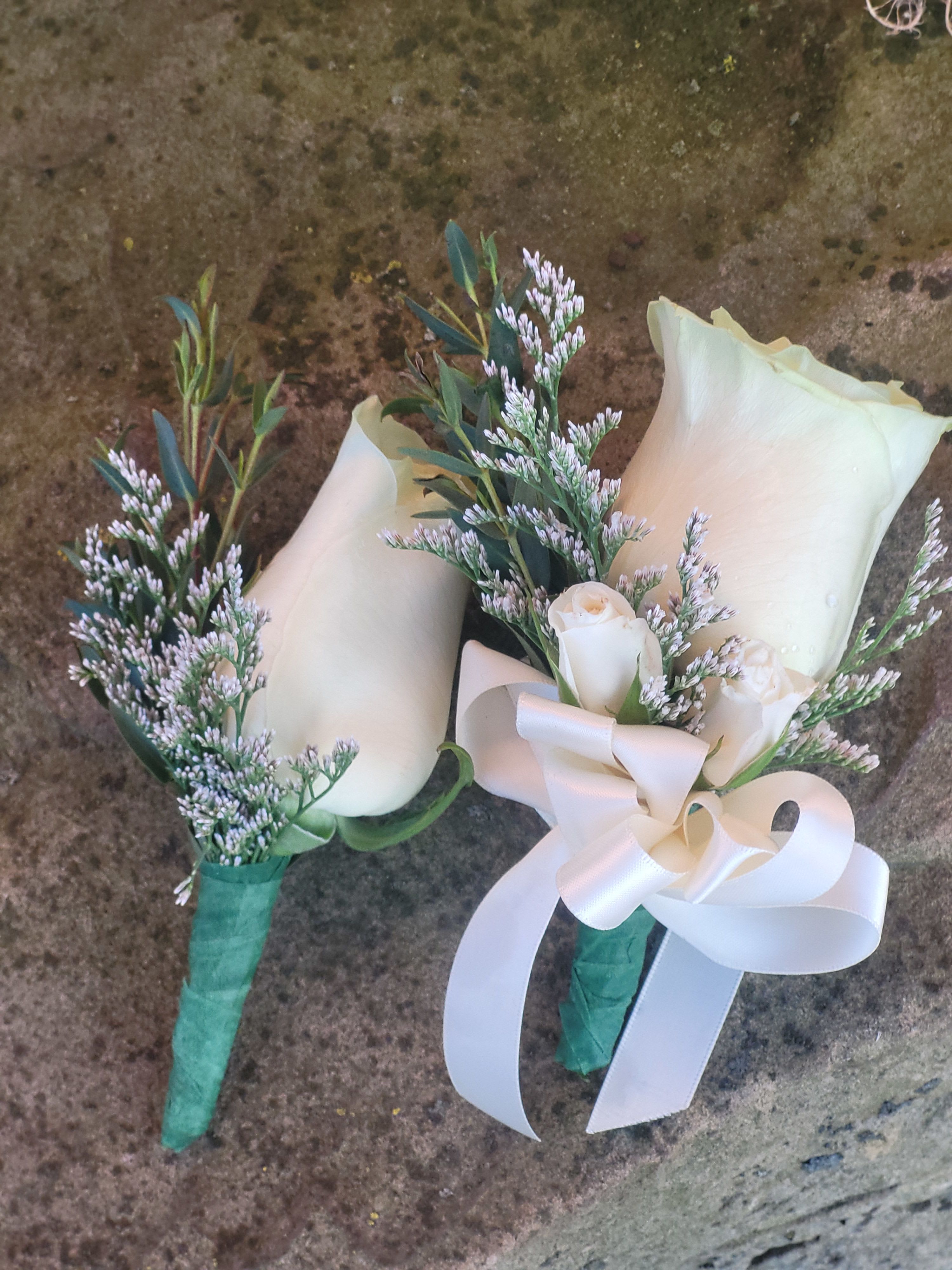 Two small white rose boutonnieres with greenery and ribbon