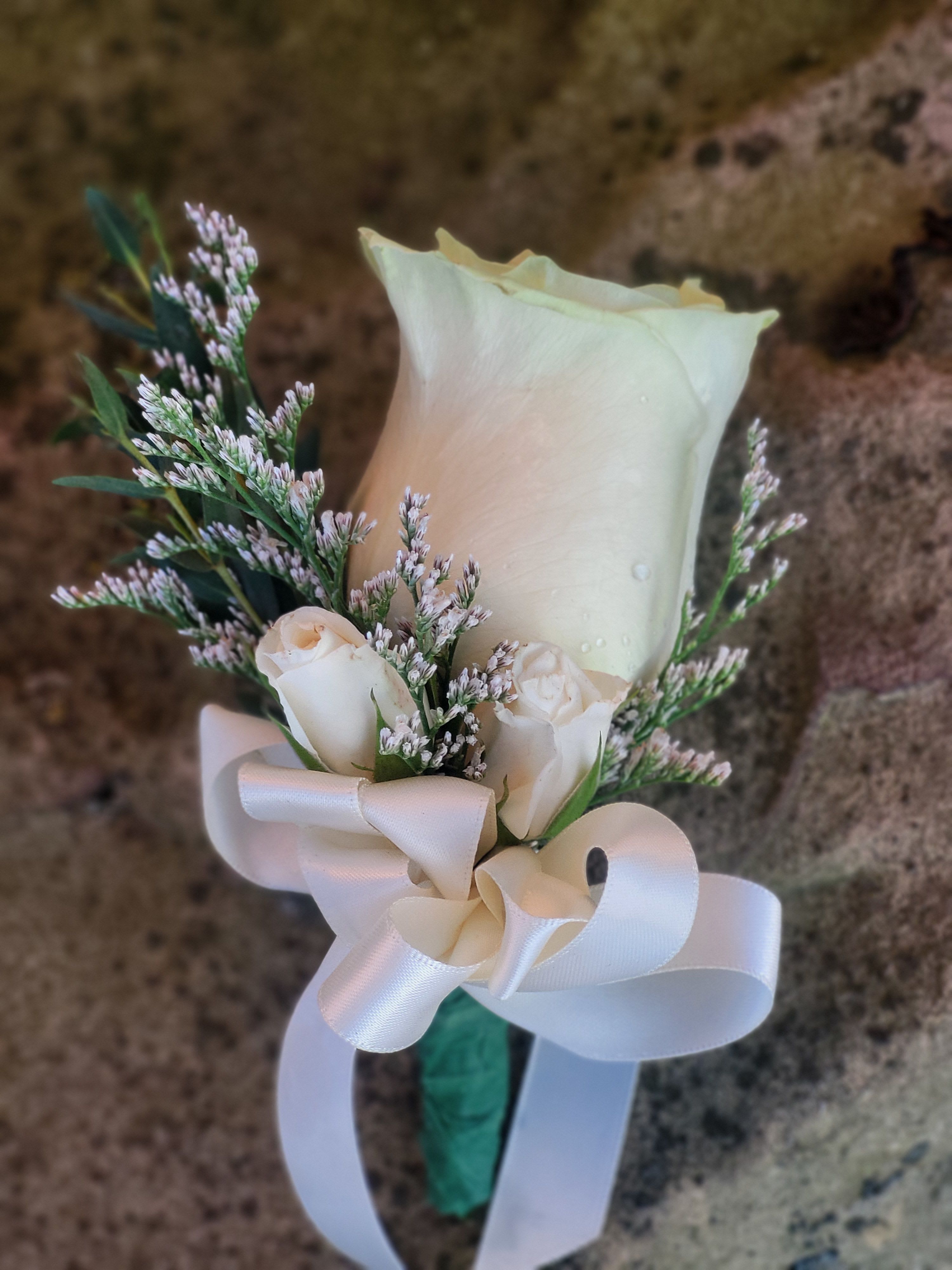 White rose boutonniere with small filler flowers and a satin ribbon bow