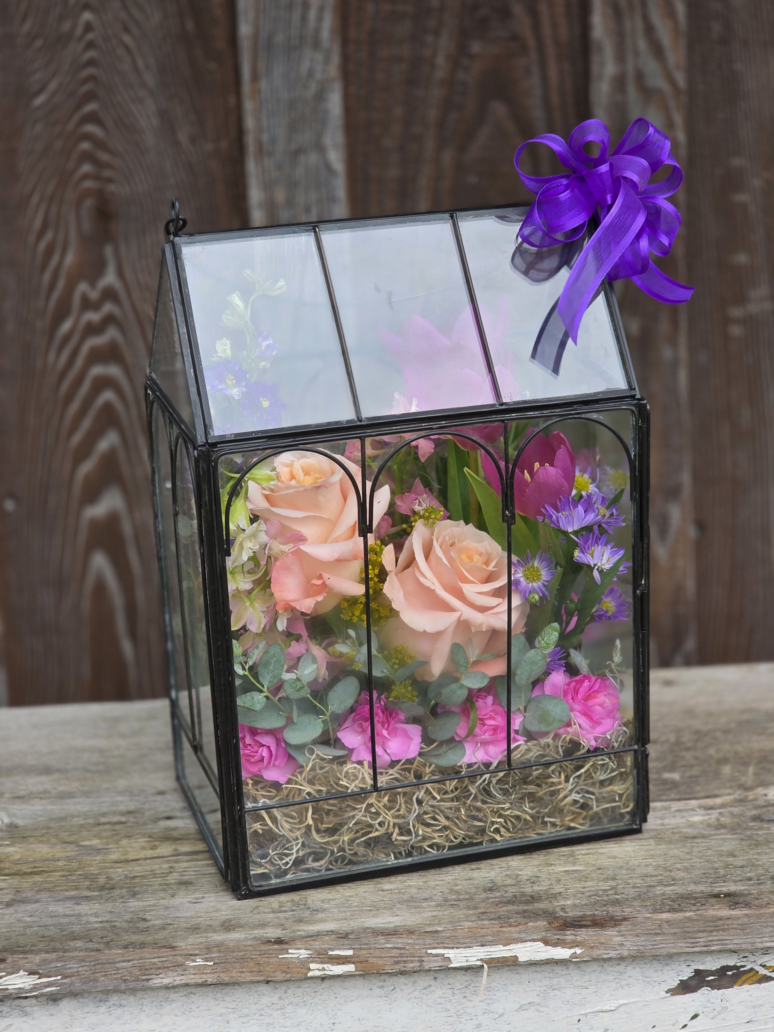 Floral arrangement in a glass lantern box with a purple ribbon bow