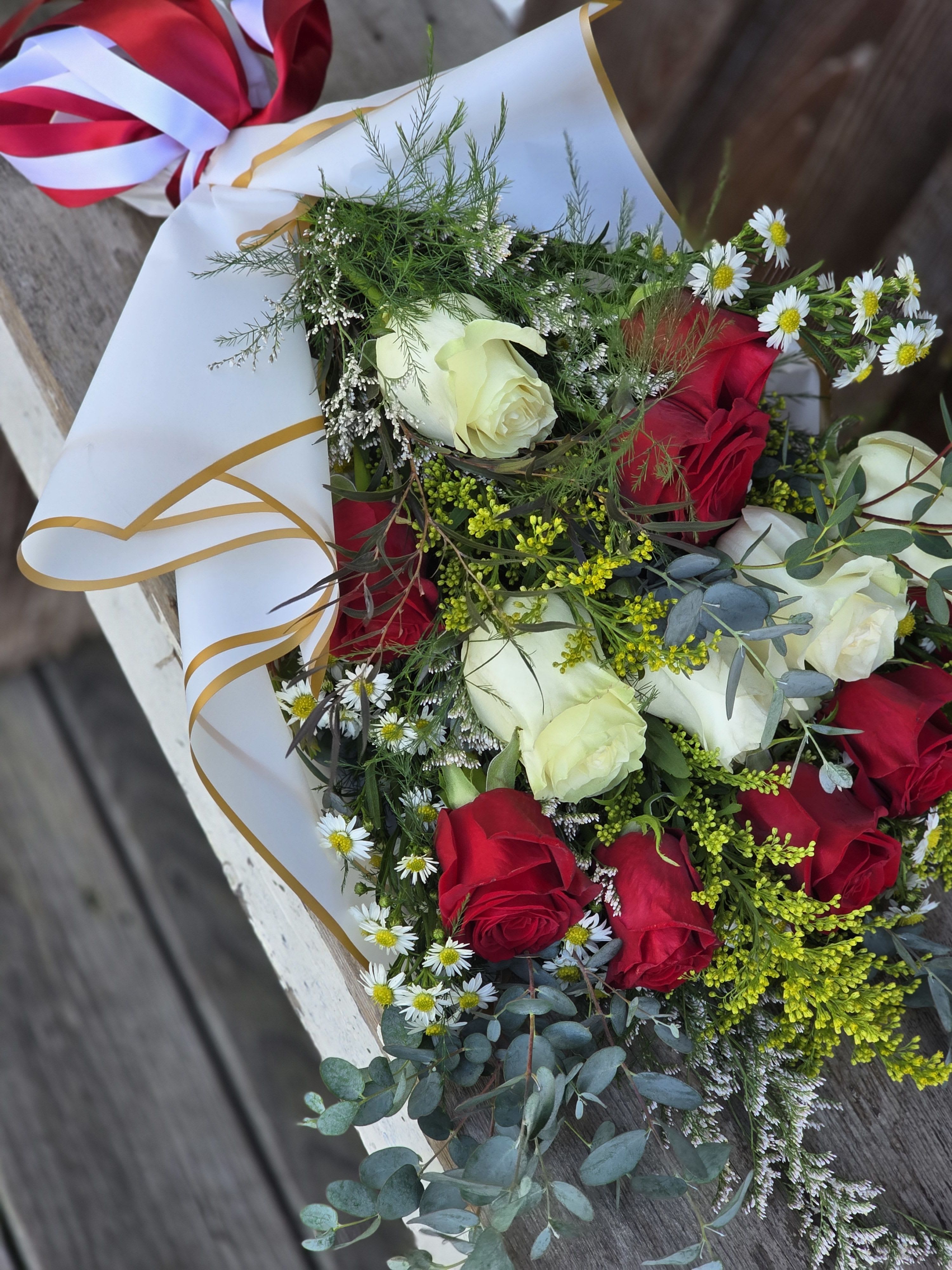 Bouquet of red and white roses with small daisies in white wrap