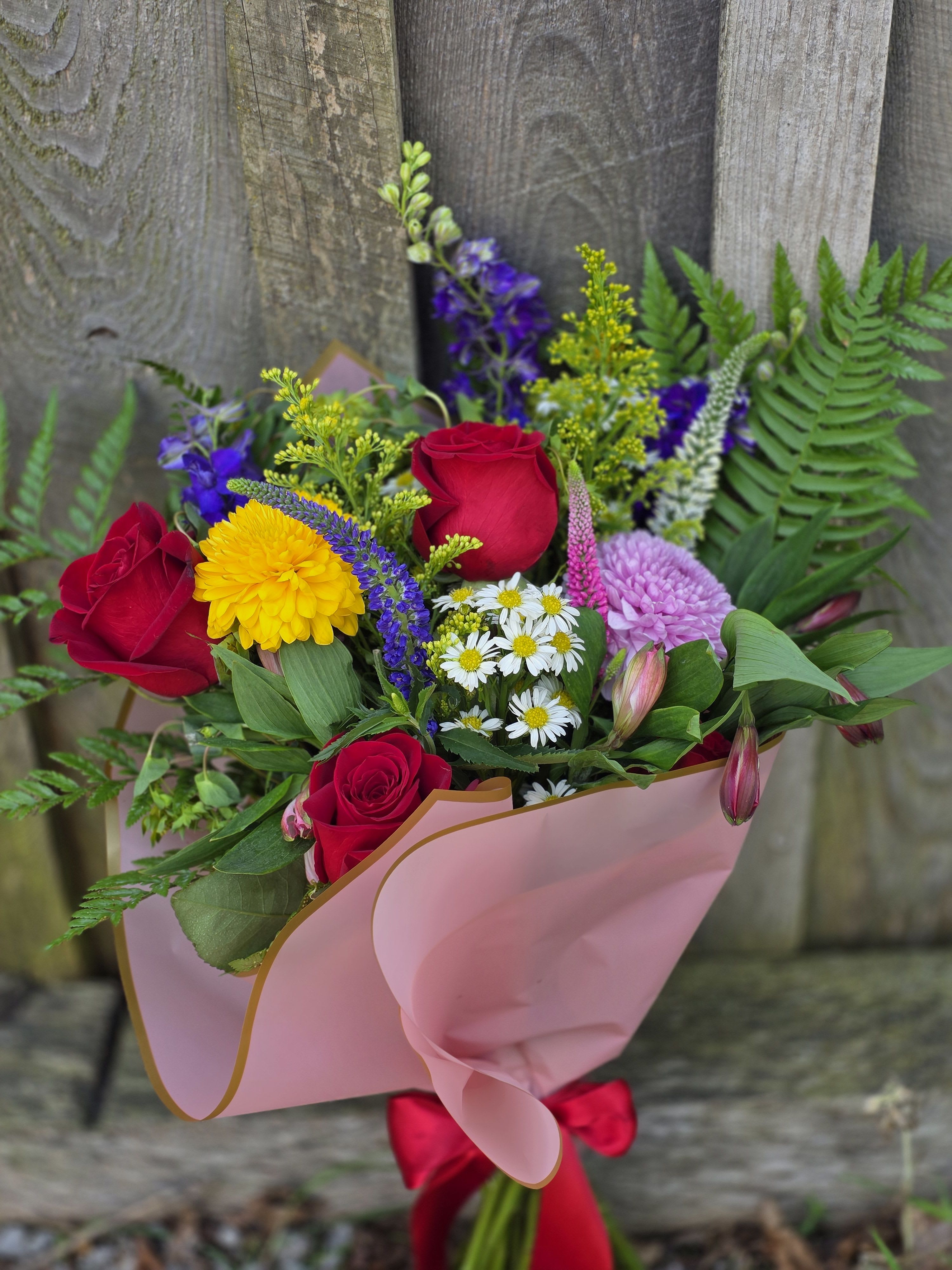 Bouquet of red roses, yellow blooms, and purple flowers wrapped in pink paper