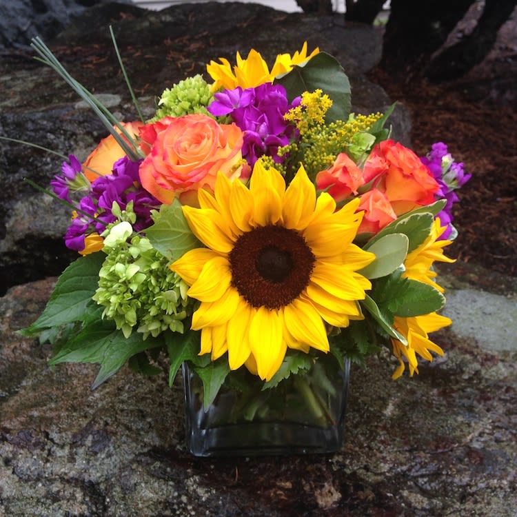 Bright mixed bouquet with sunflowers, roses, and purple flowers in a glass vase