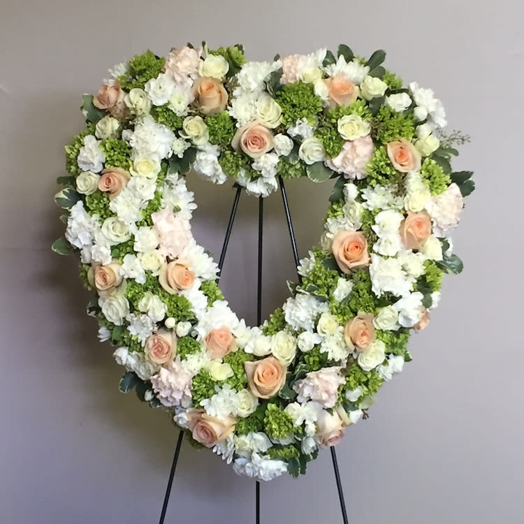 Heart-shaped floral wreath with white and peach roses on a stand