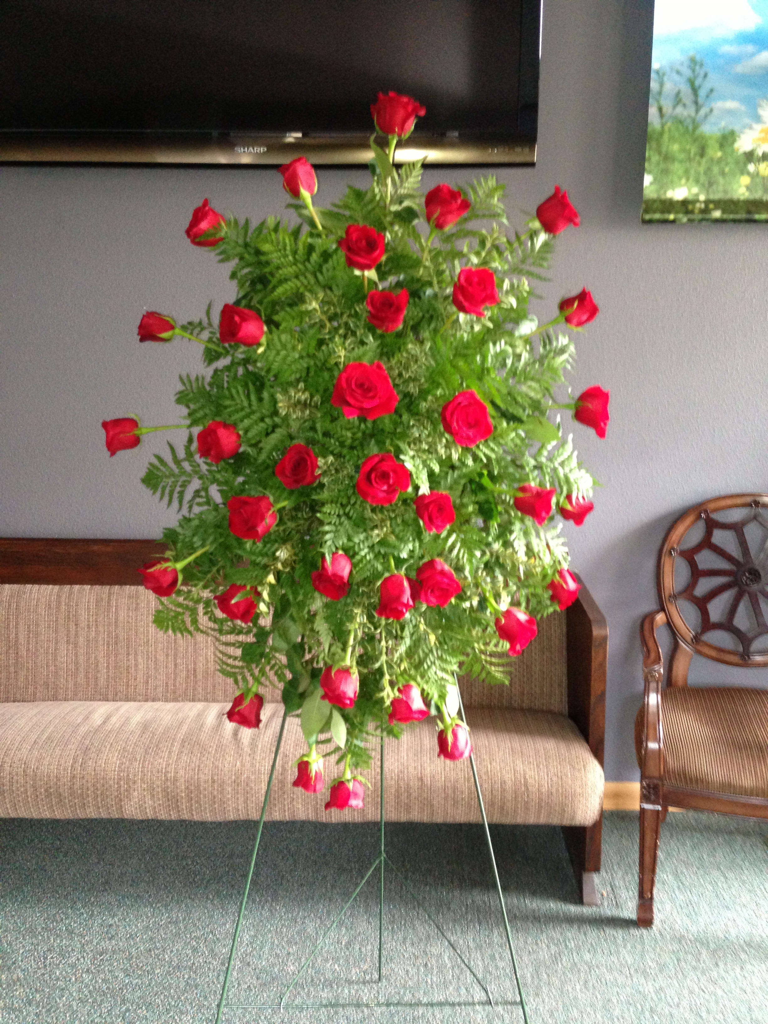 Tall standing arrangement of red roses and greenery on a metal easel