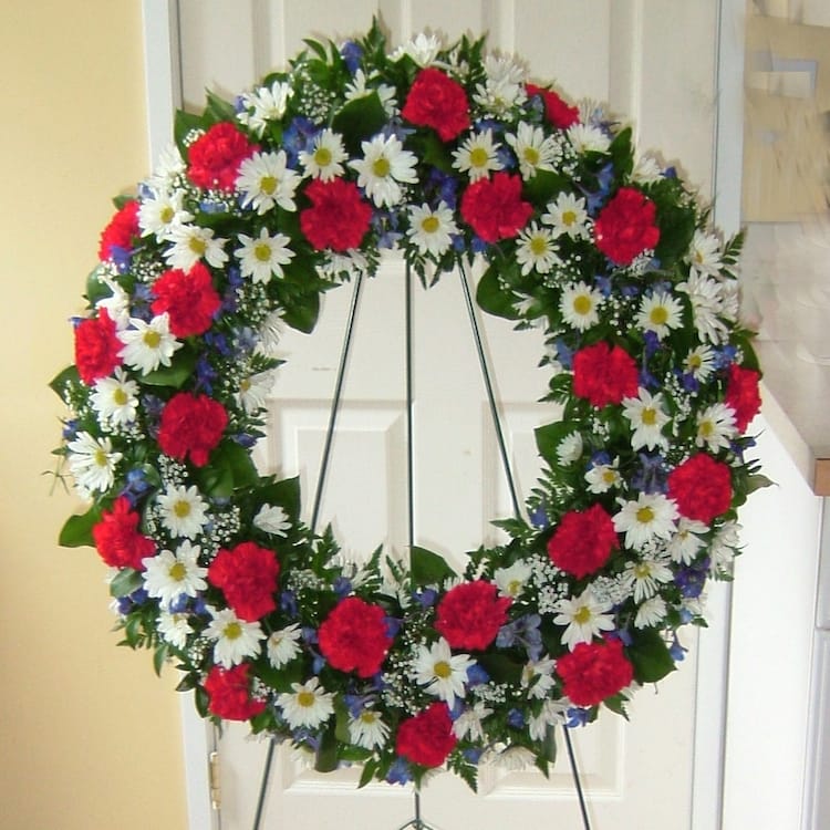 Circular floral wreath with red carnations and white daisies on a stand