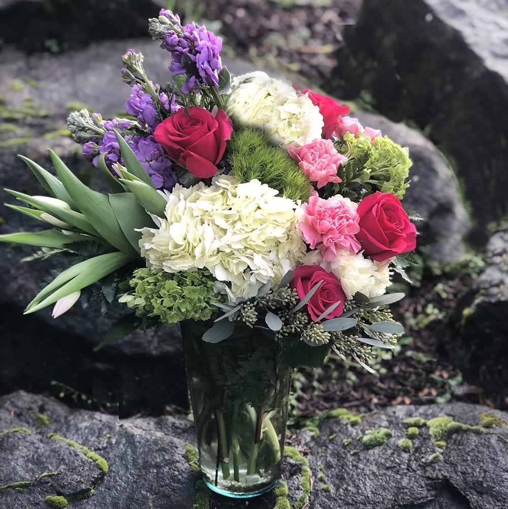 Bouquet of roses, hydrangeas, and purple flowers in a glass vase