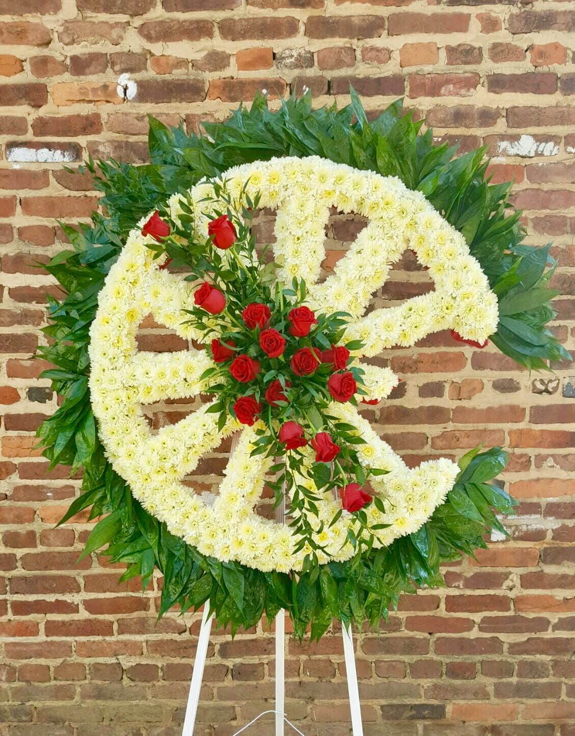Large floral wreath with white flowers and red roses on a stand