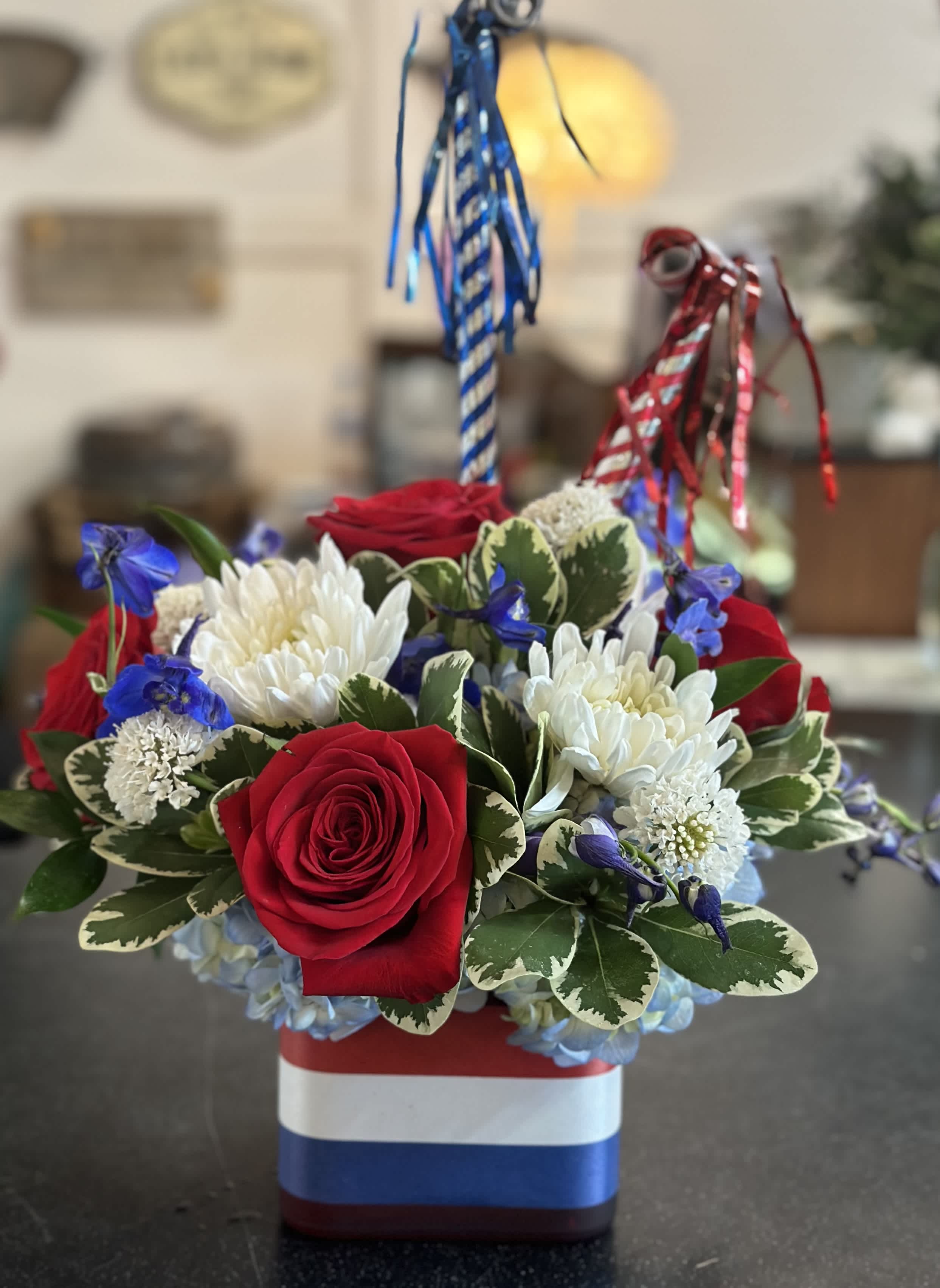 Red roses and white chrysanthemums in a patriotic striped container with blue and red ribbons