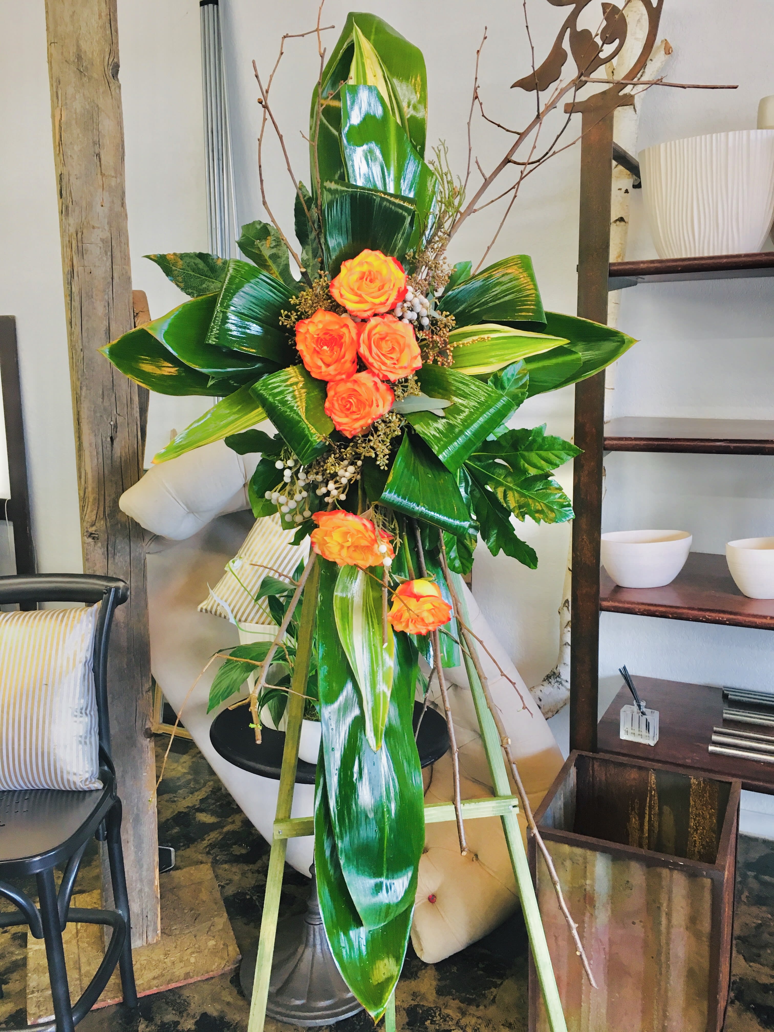 Tall floral standing arrangement with orange roses and glossy tropical leaves
