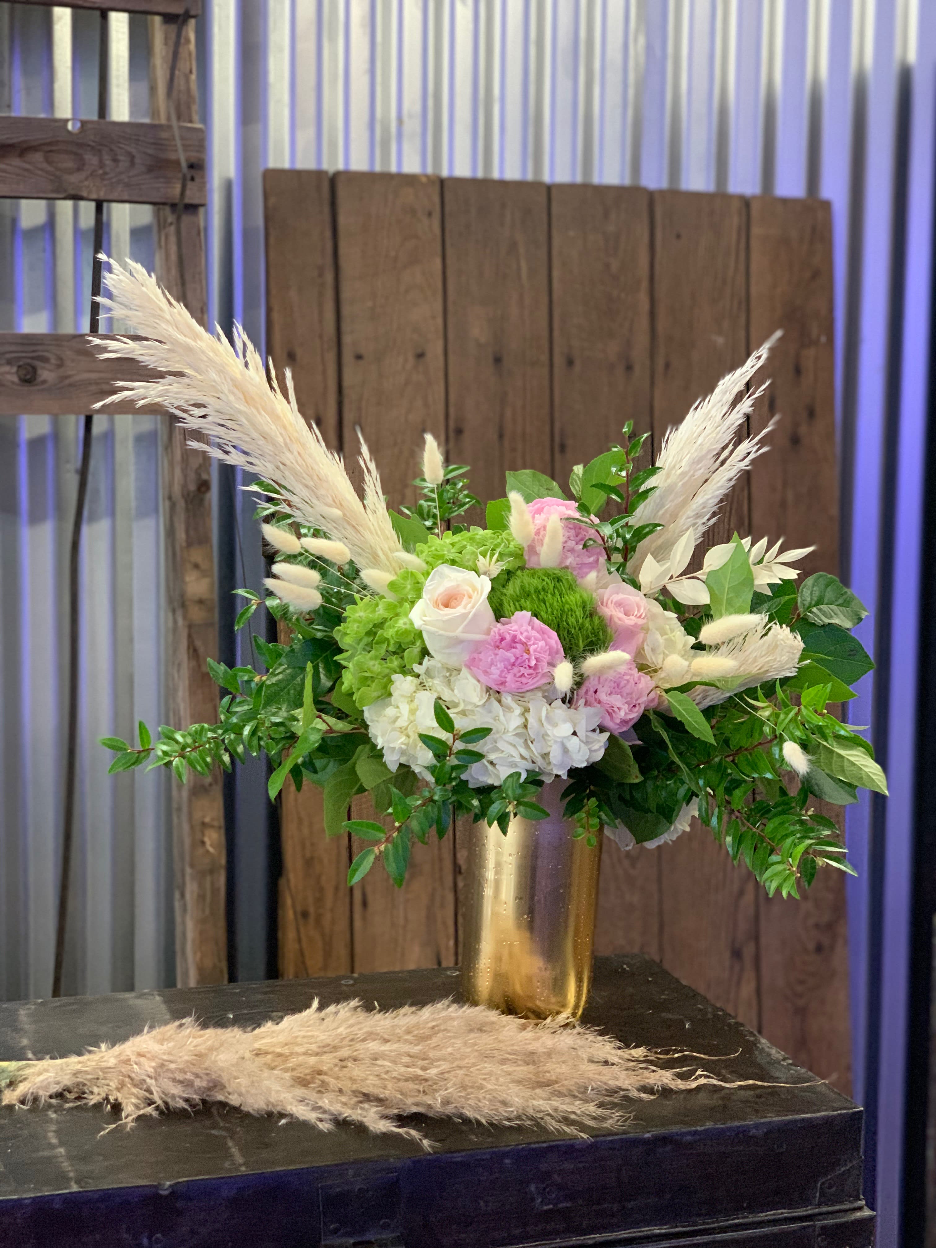 Pink and white floral arrangement in a gold vase with pampas grass