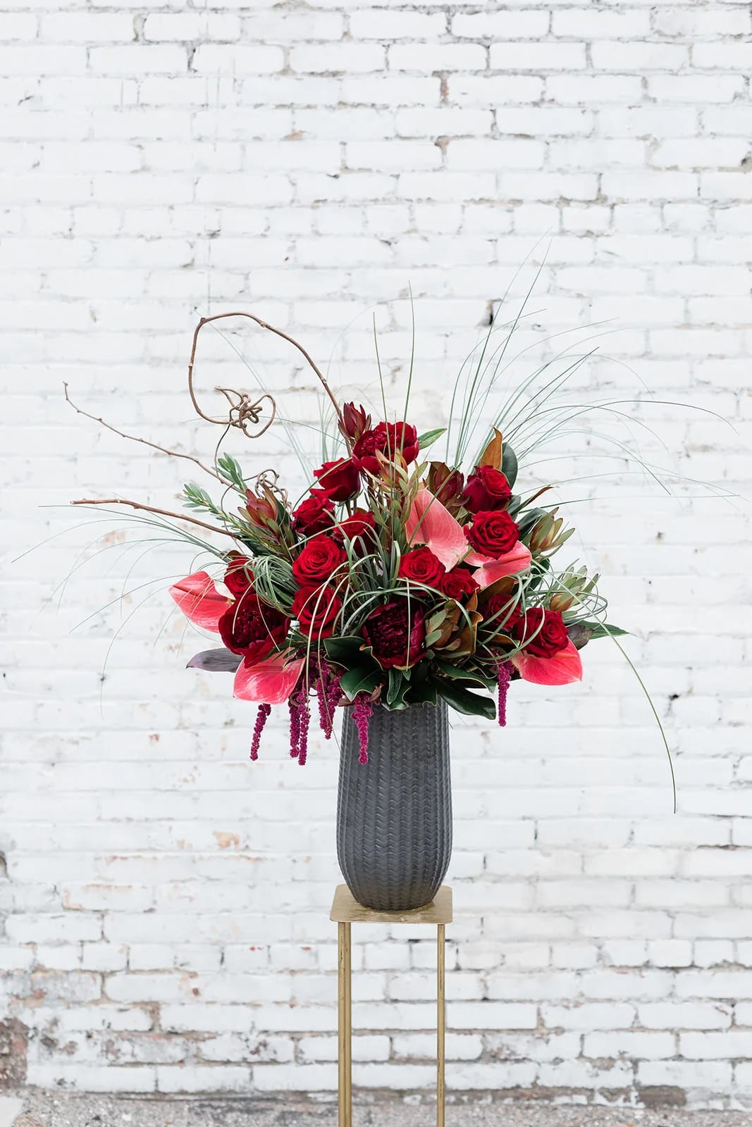 Tall red floral arrangement in a dark vase on a stand