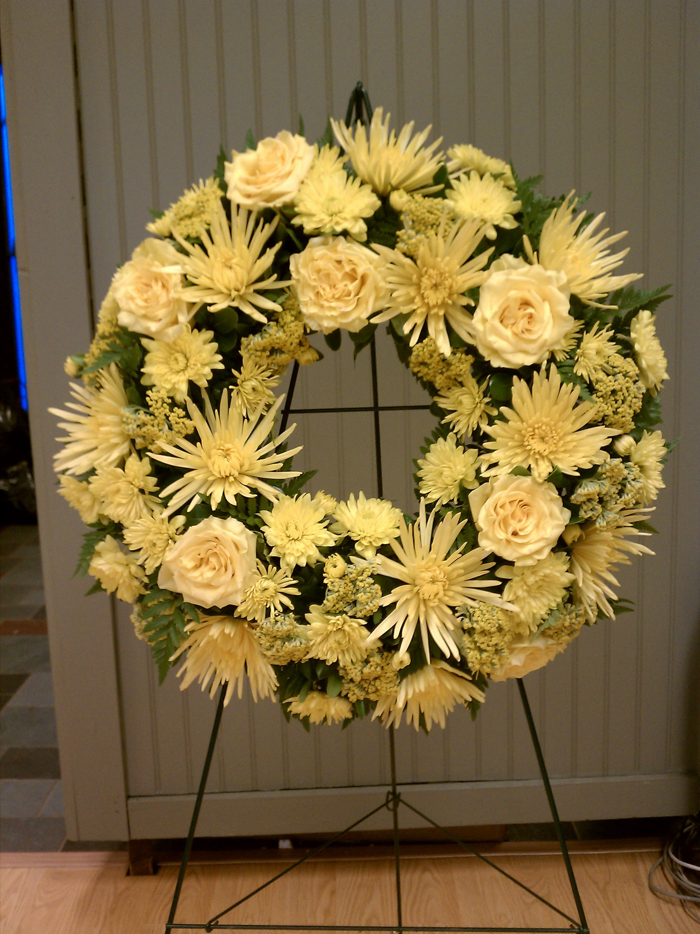 Standing wreath of pale yellow roses and mums on a metal easel