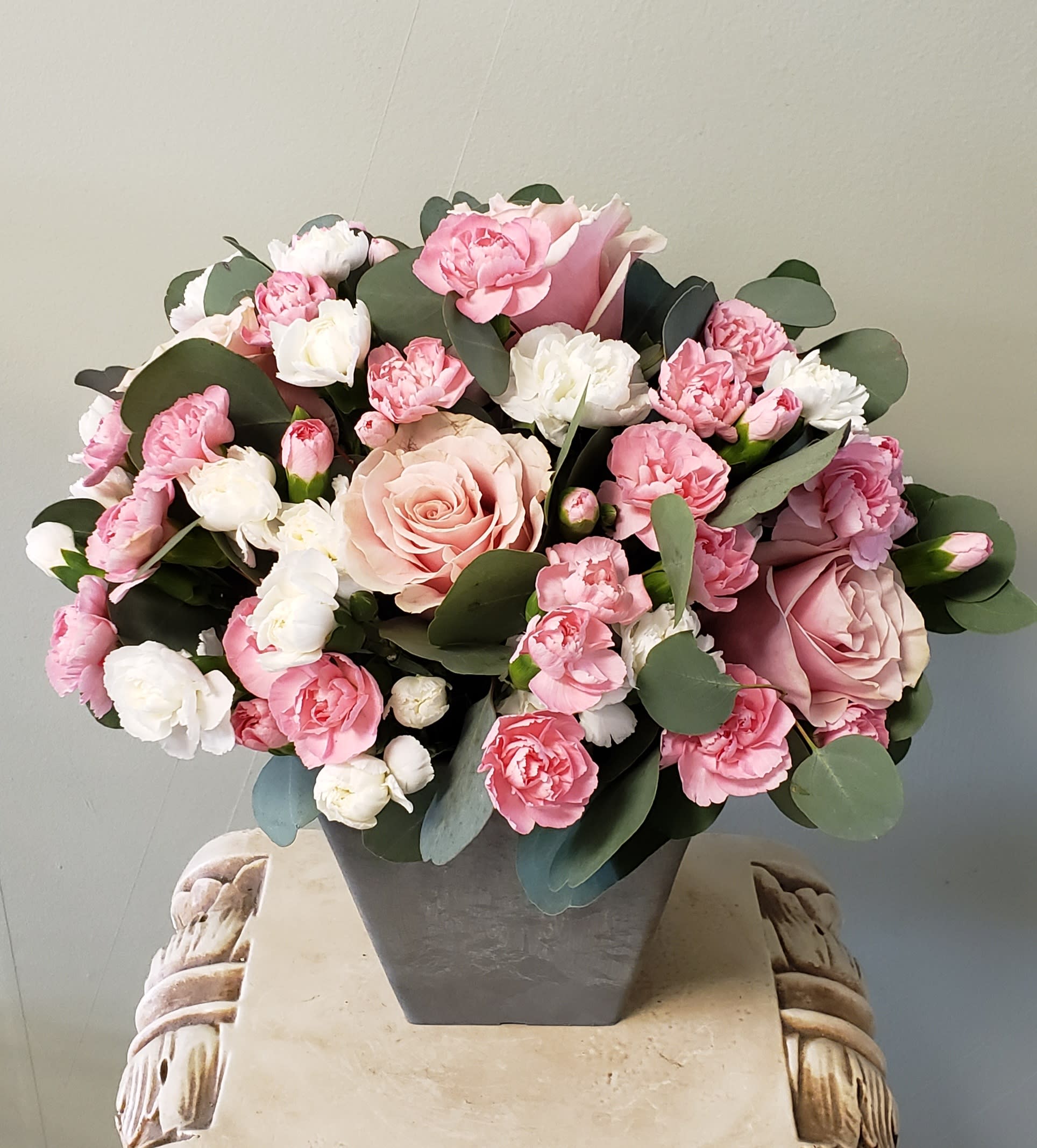 Pink and white roses and carnations arranged in a gray square vase