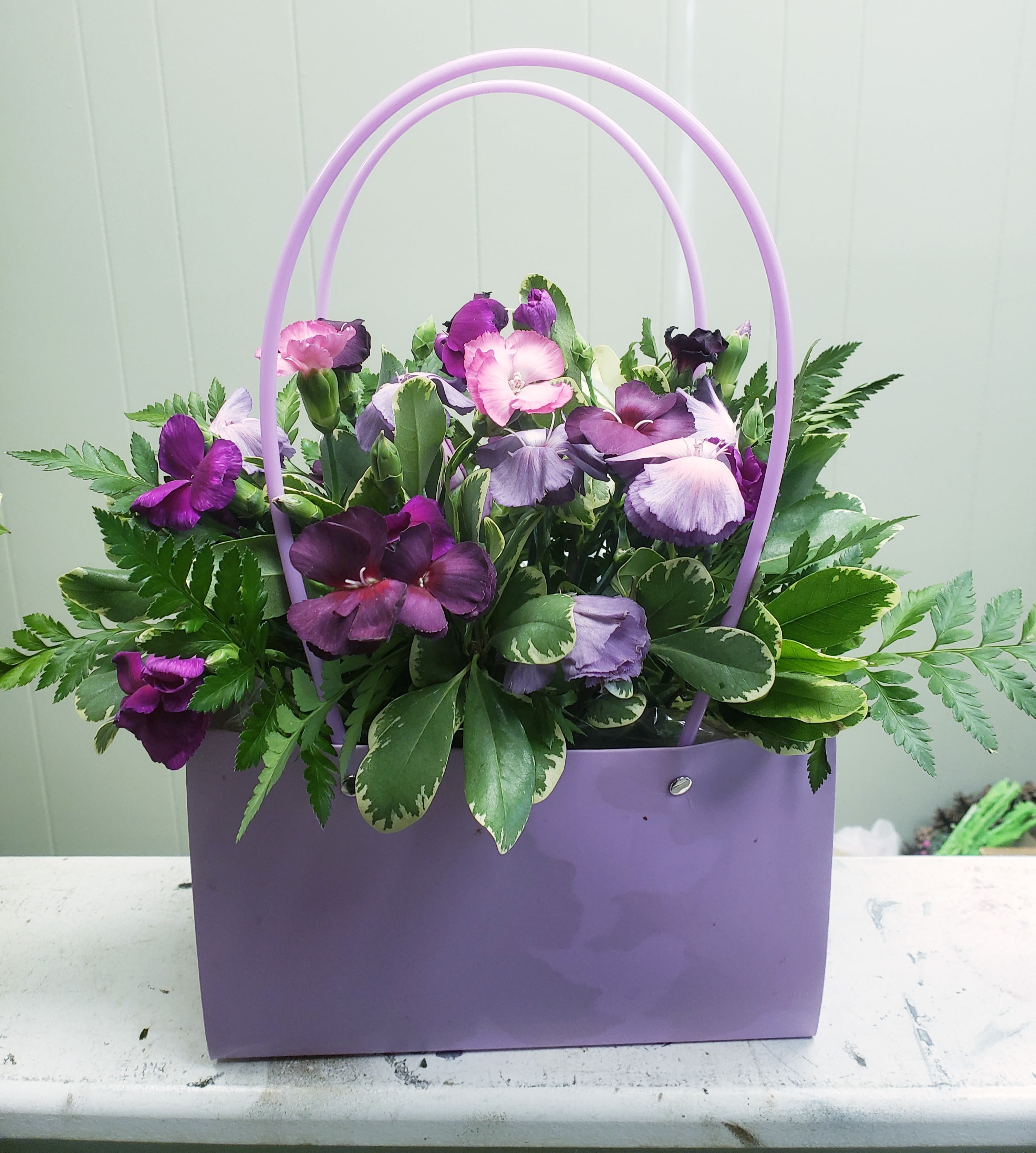 Purple and lavender flowers in a lavender handbag-style container with double handles