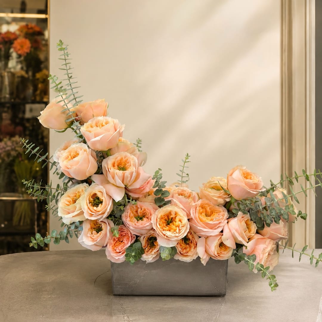 Peach roses arranged in a low rectangular vase with airy eucalyptus stems