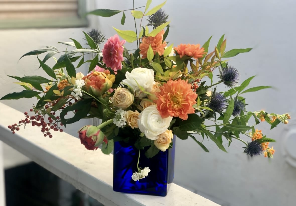 Asymmetrical bouquet of orange dahlias and cream roses in a cobalt blue glass cube vase