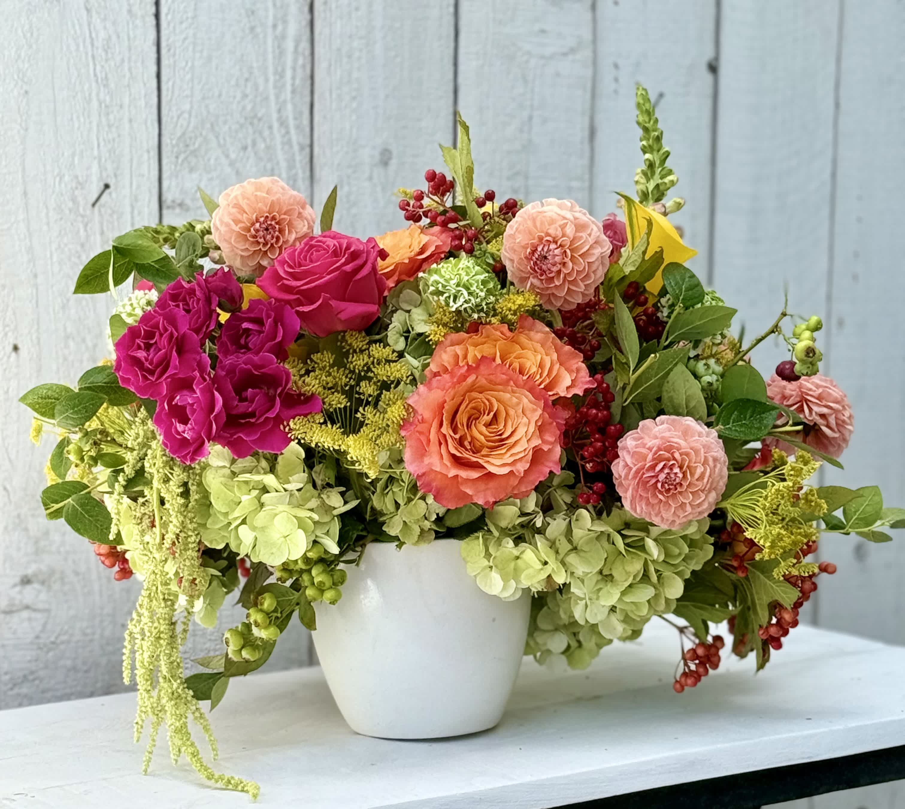 Mixed bouquet of pink, peach, and green flowers in a white pot