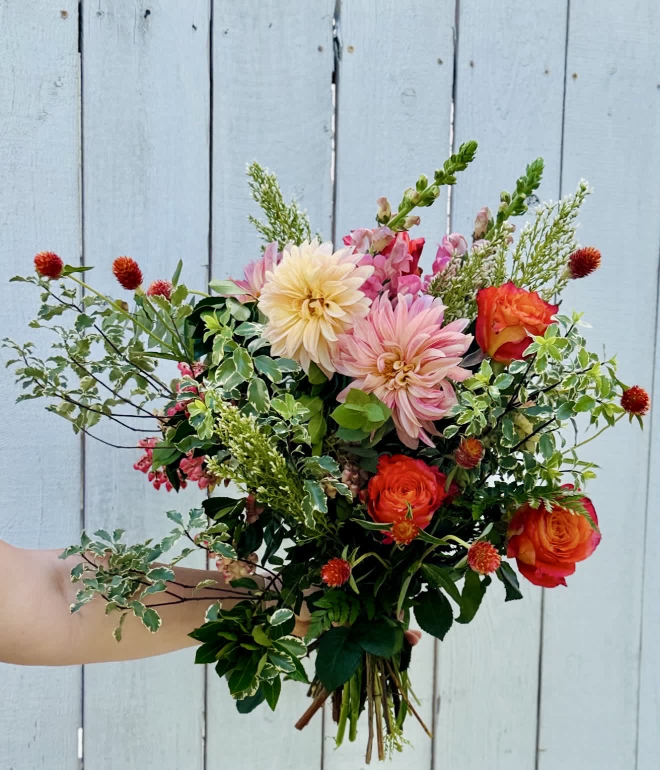 Handheld bouquet with pink and orange flowers against a pale blue fence
