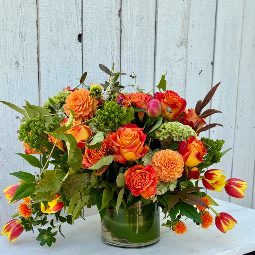 Bright mixed bouquet of orange and red flowers in a glass vase