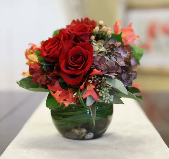 Red roses and hydrangeas arranged in a green glass vase
