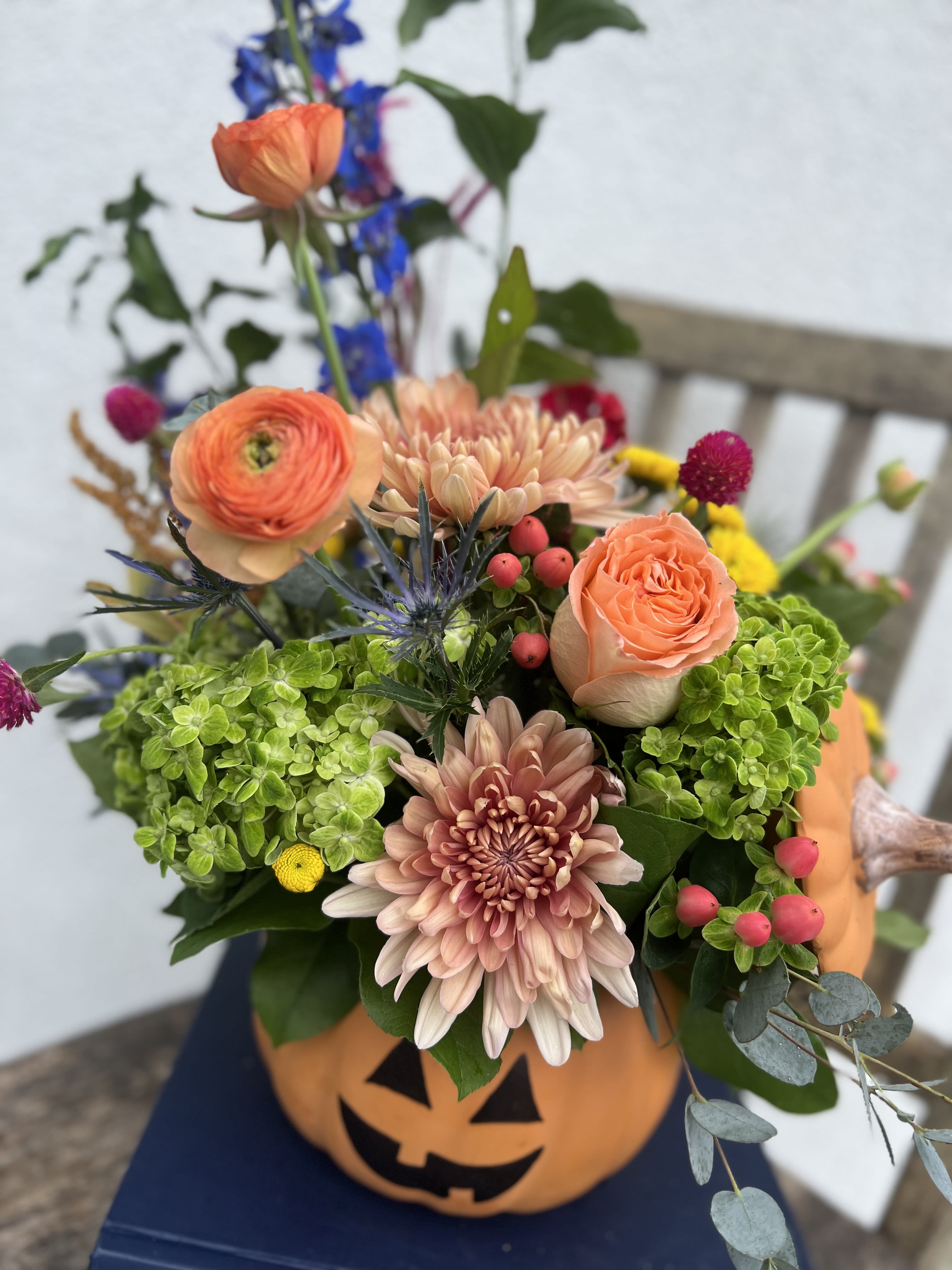 Jack - A scary good floral arrangement to welcome in the spooky season! Featuring roses, ranunculus, delphinium, autumnal textures, hydrangeas and a mix of fall accent flowers, arranged in a jack o' lantern ceramic vase.
