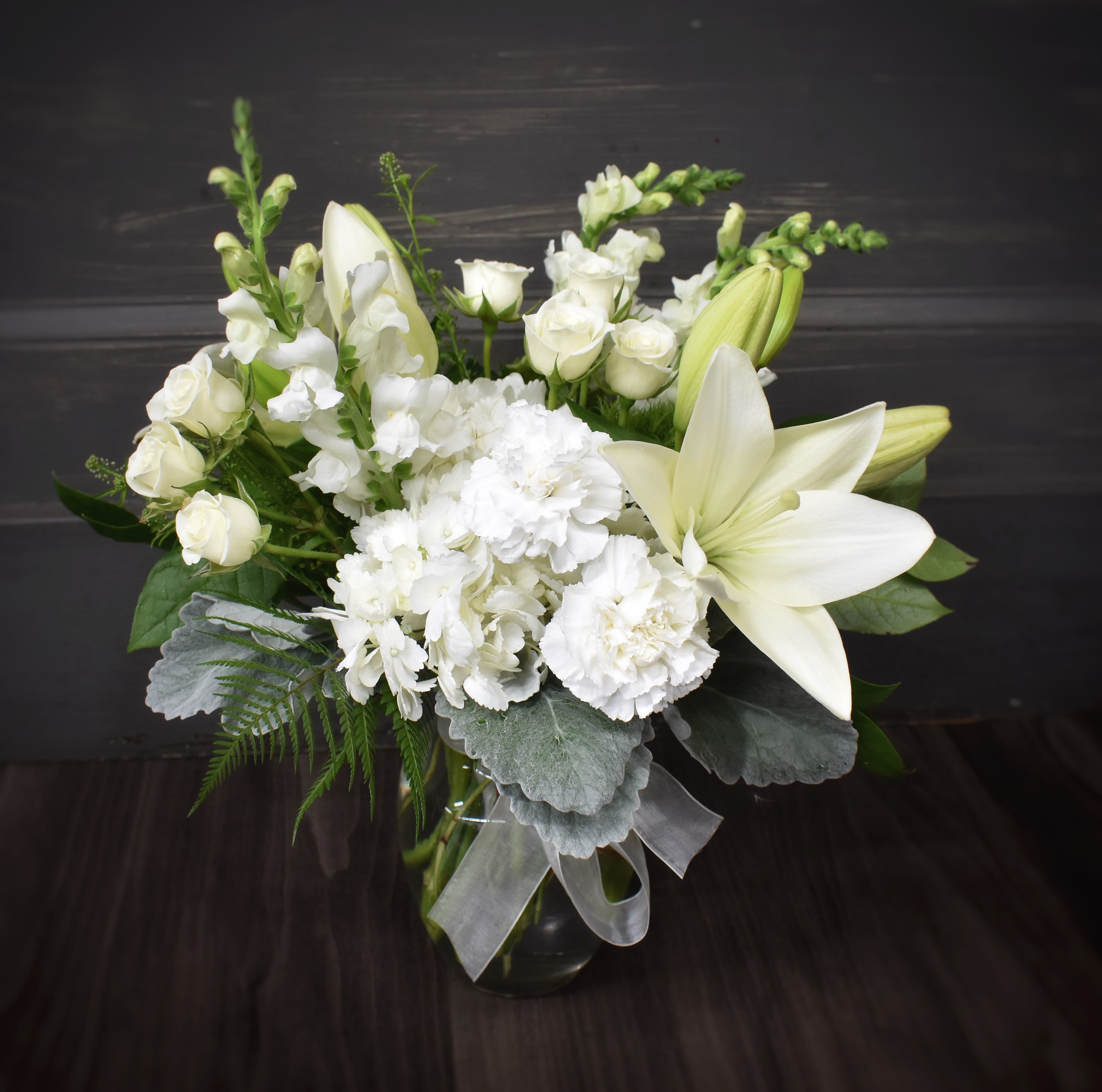 White lilies and roses arranged in a glass vase with silver ribbon