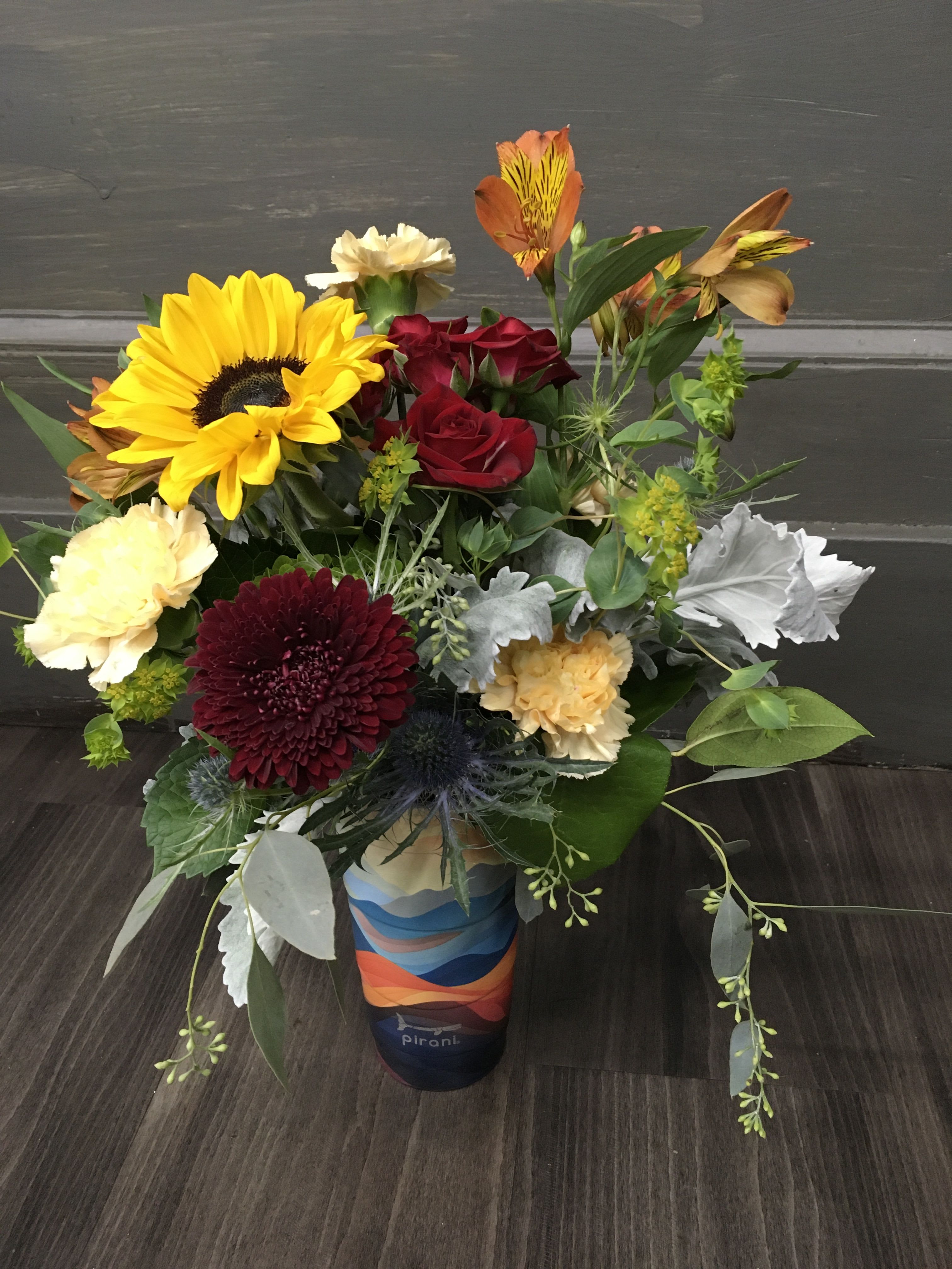 Mixed bouquet with sunflowers, red roses, and carnations in a colorful vase