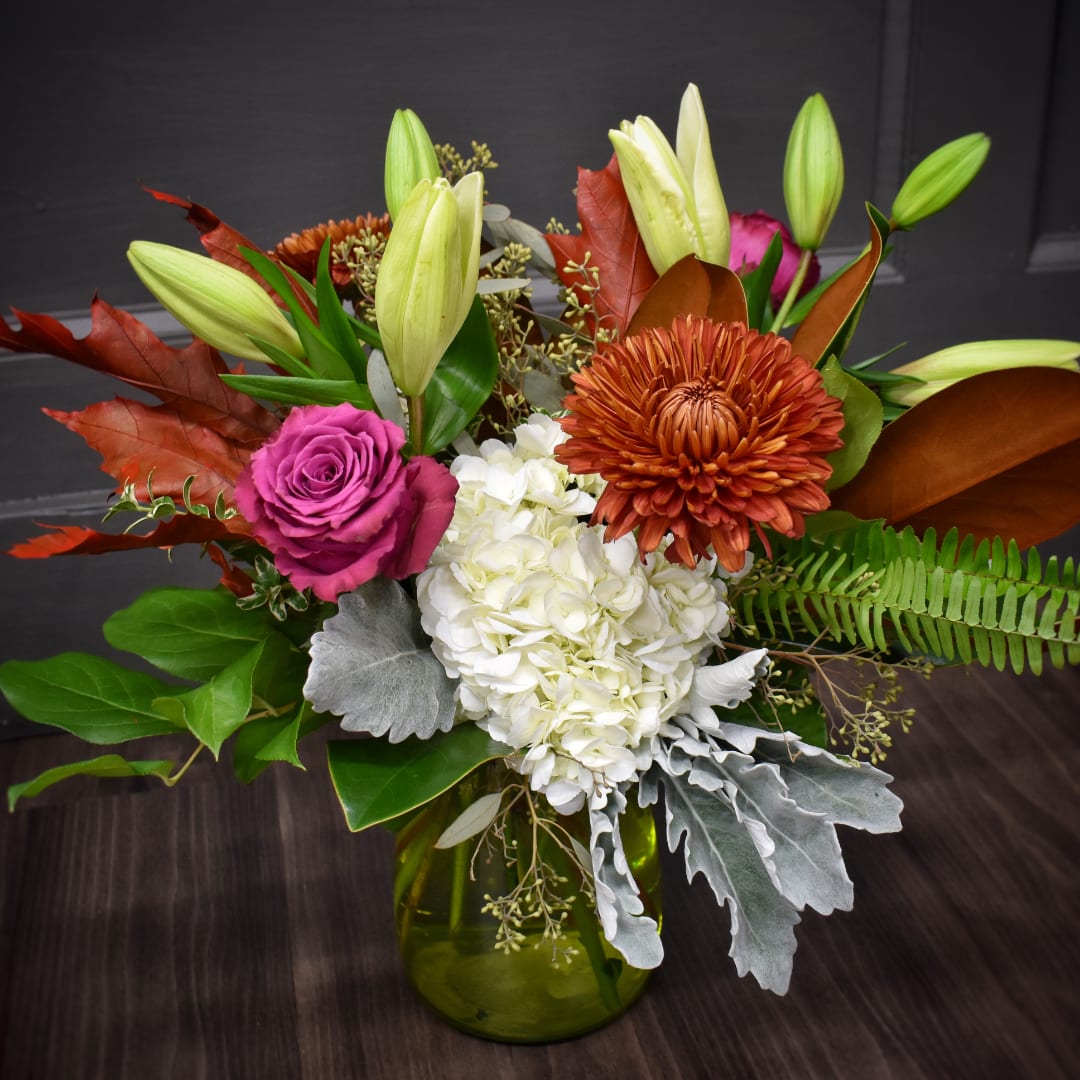 Mixed bouquet with lilies, roses, hydrangea, and chrysanthemum in a green glass vase