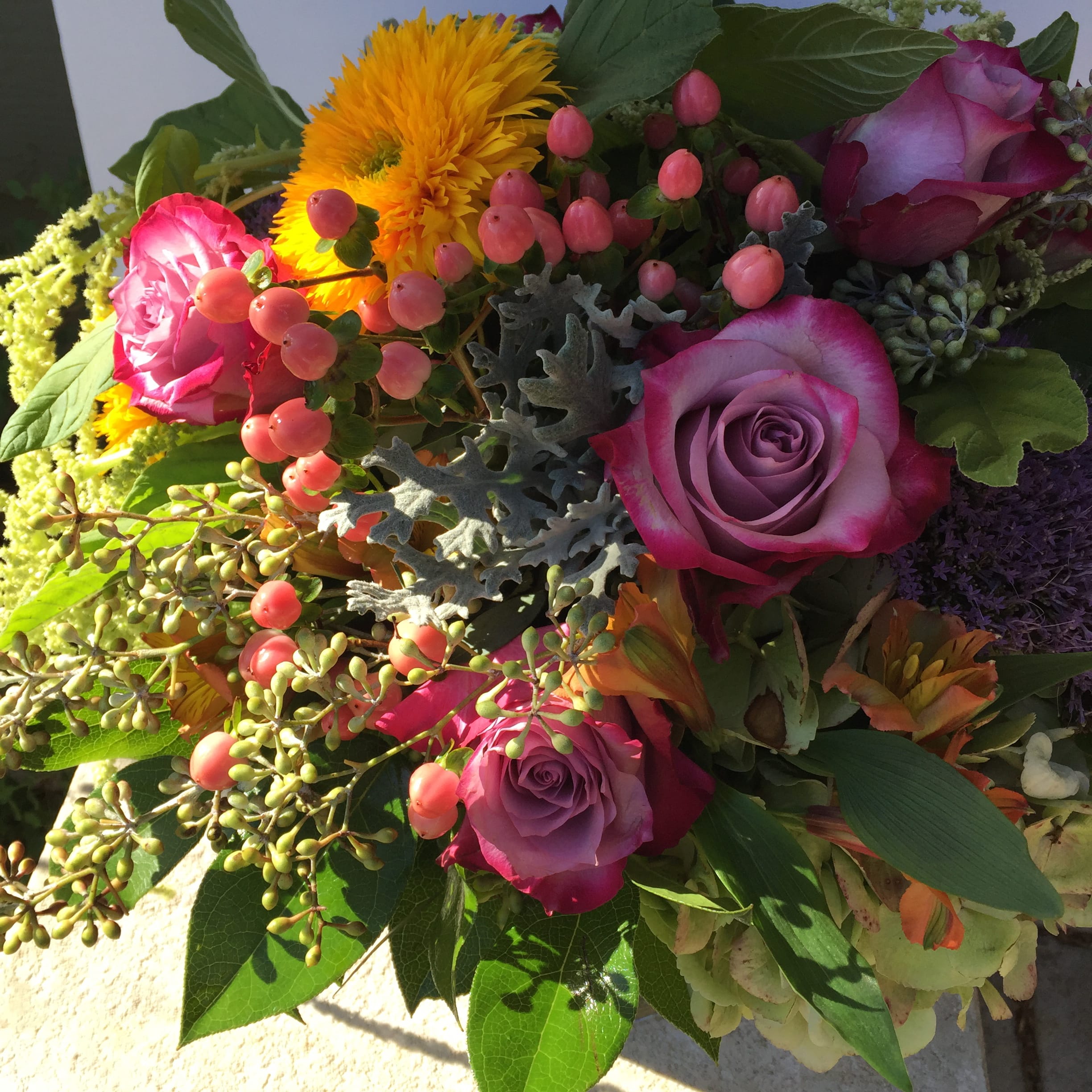 Bouquet of purple and pink roses with yellow blooms and berry accents