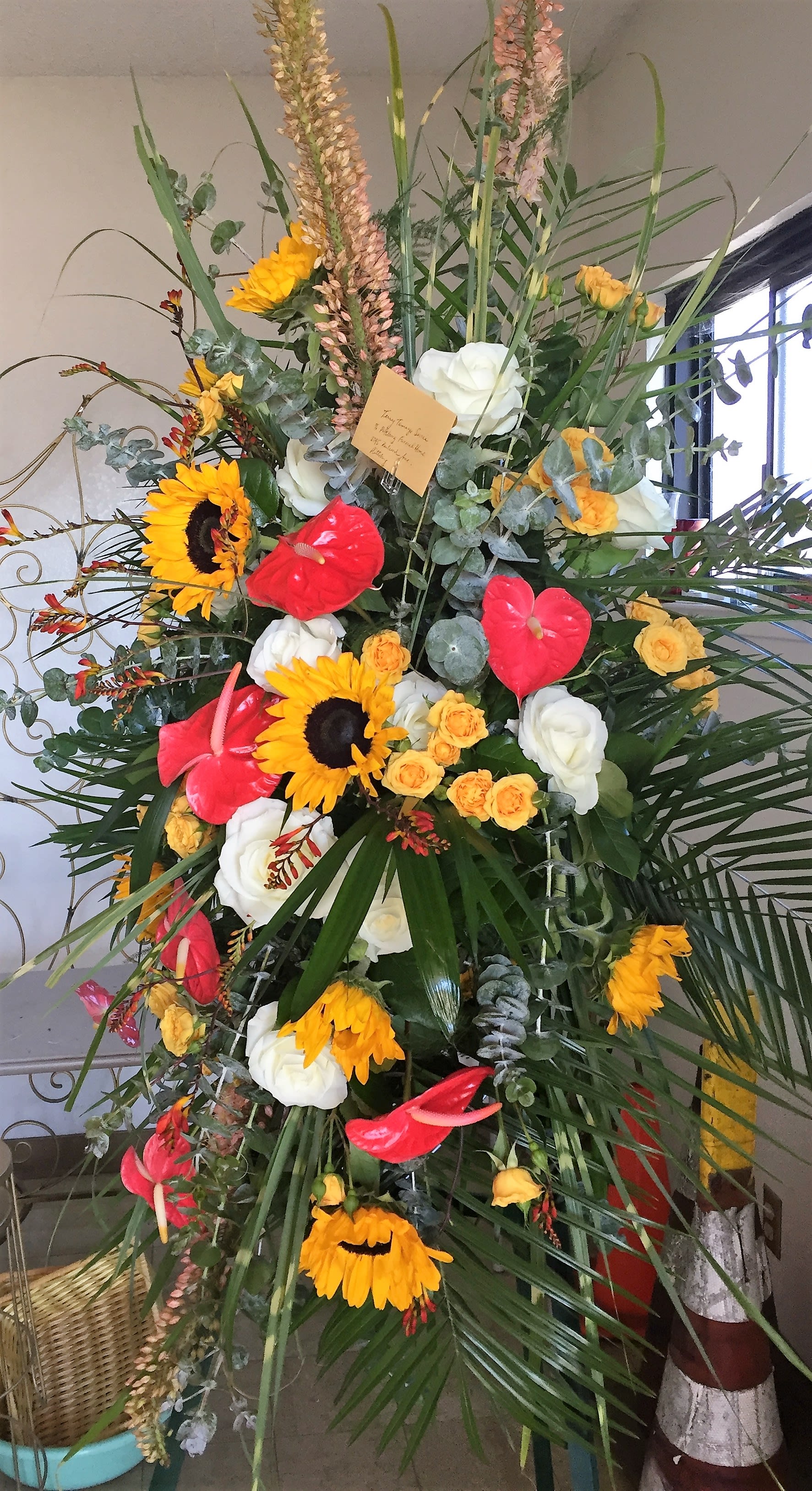 Tall floral standing spray with sunflowers, roses, and red anthuriums