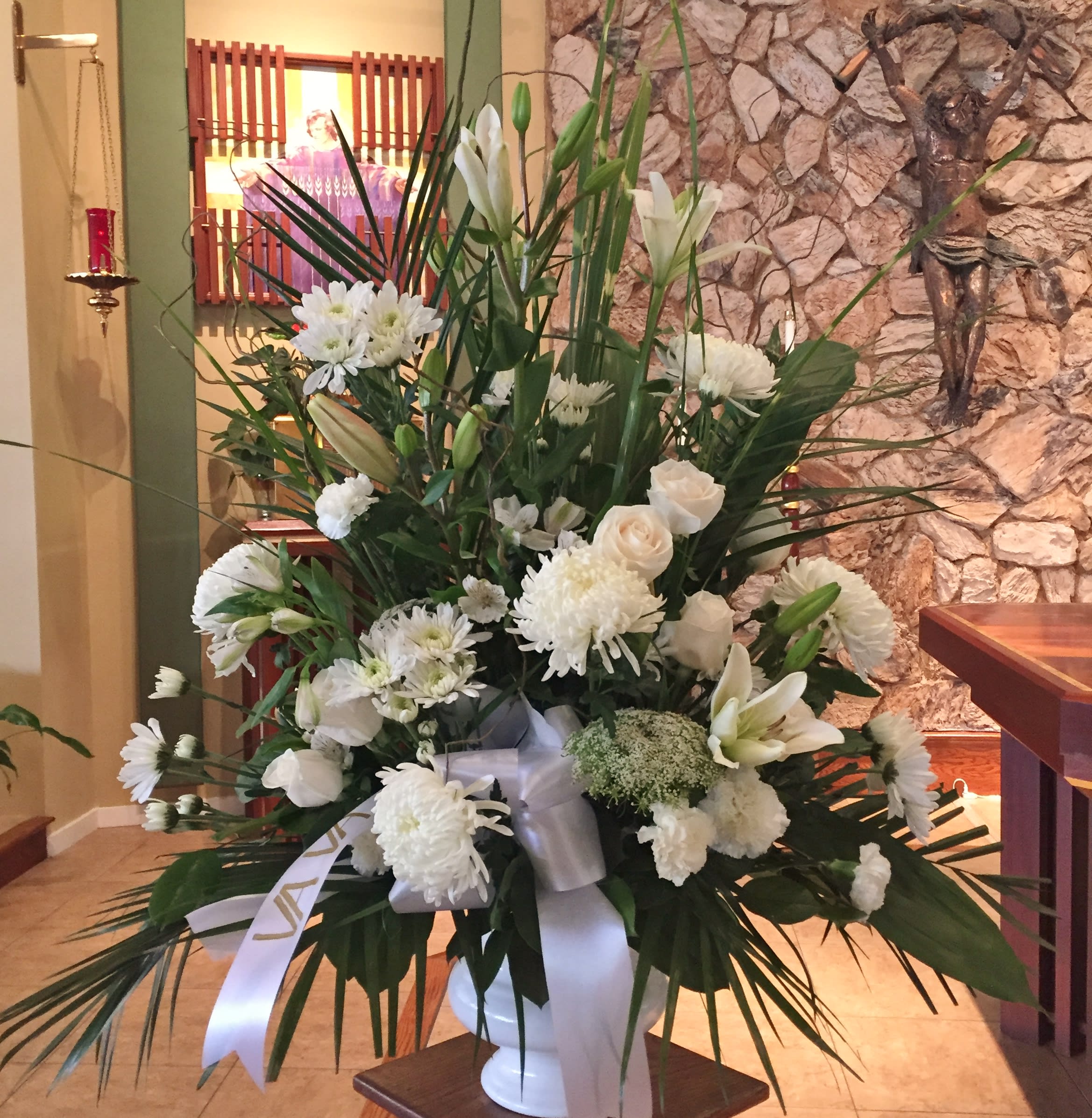 Tall white floral arrangement in a white vase with a ribbon bow