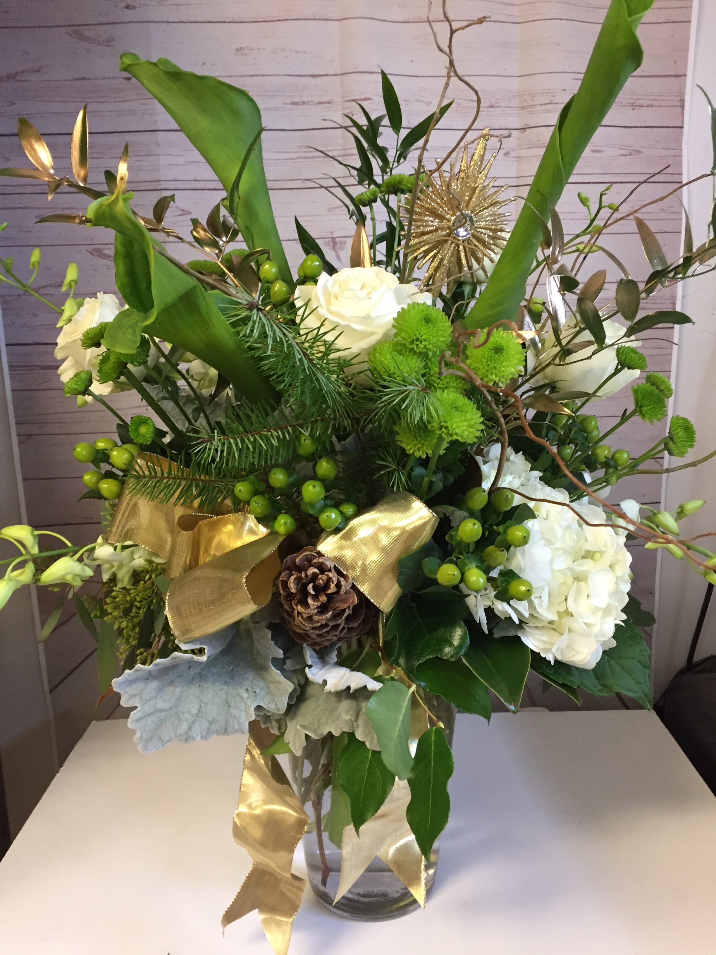 Green and white floral arrangement in a glass vase with gold ribbon