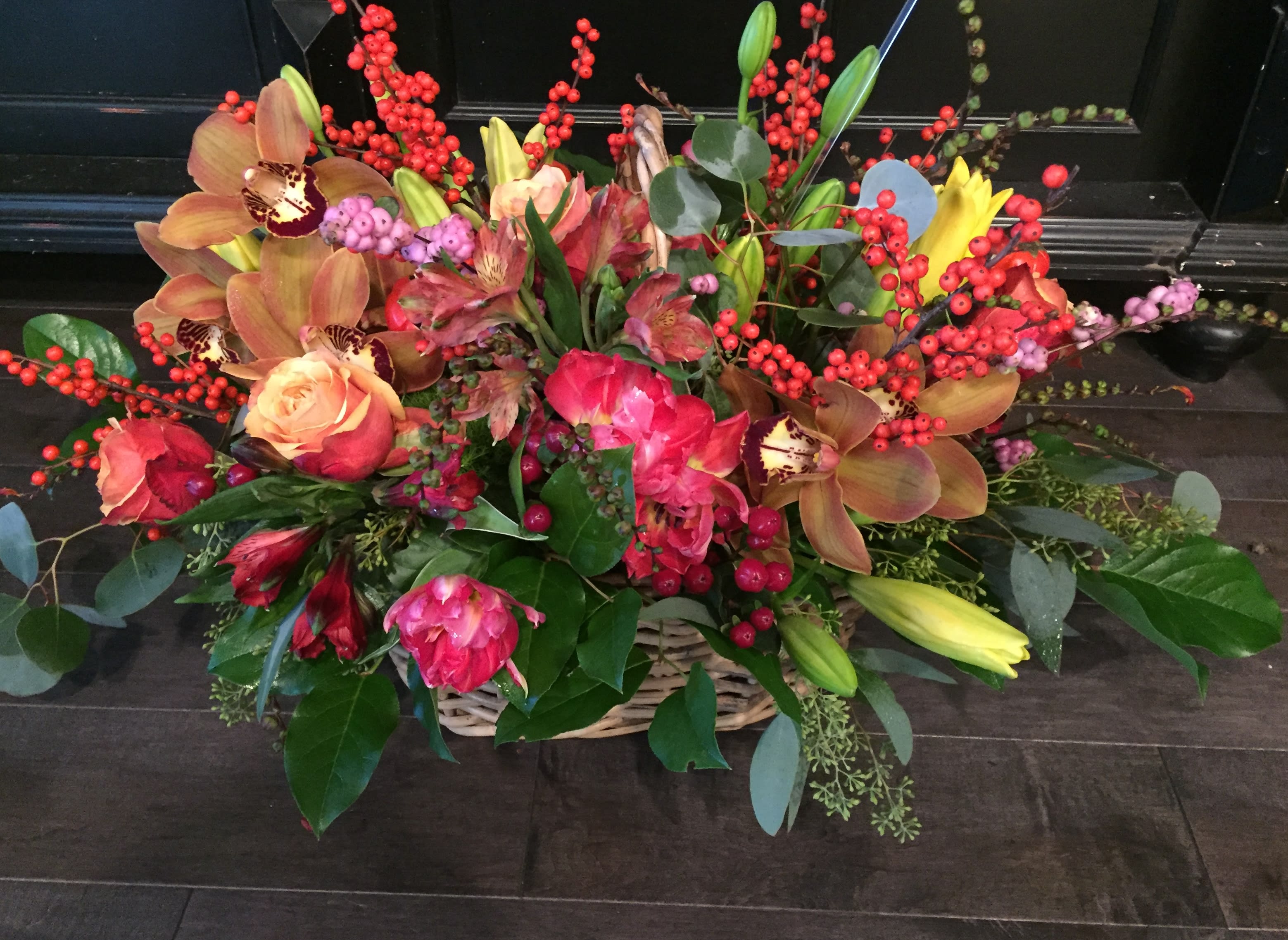 Basket arrangement of roses, orchids, lilies, and red berry stems