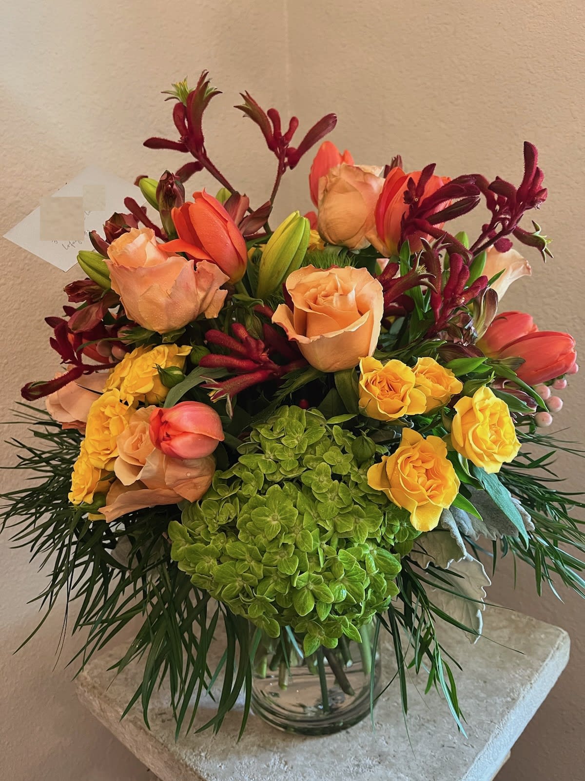 Mixed bouquet of peach roses, yellow roses, and red tulips in a glass vase