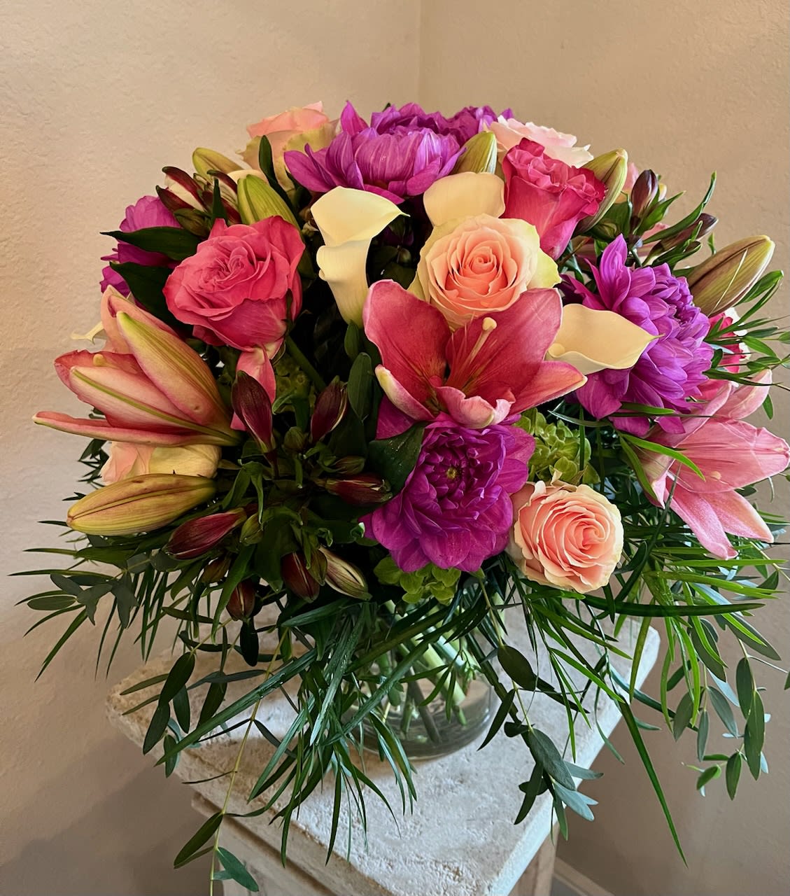 Mixed bouquet of pink lilies, roses, calla lilies, and purple blooms in a glass vase