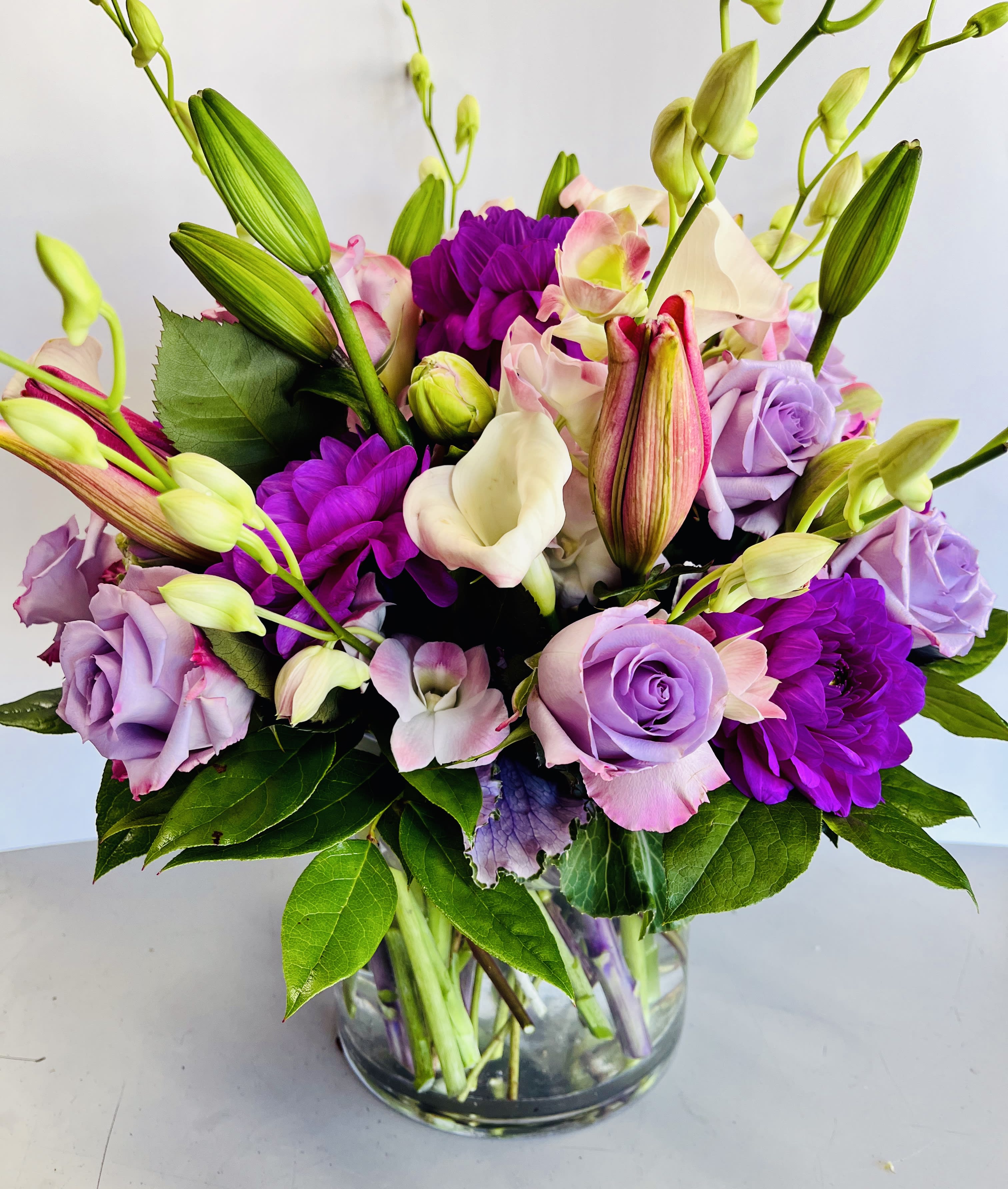 Bouquet of purple roses, lilies, and calla lilies in a glass vase