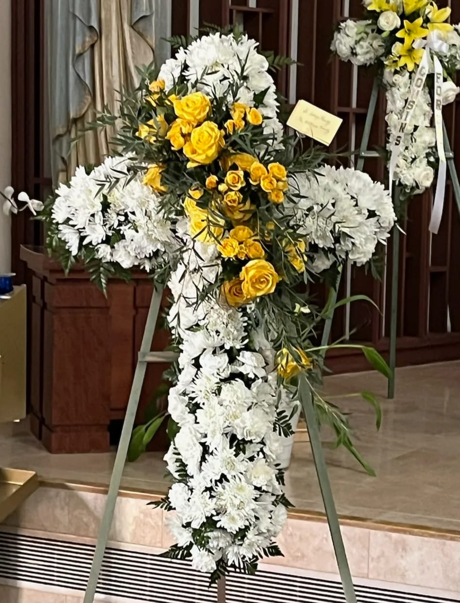 Cross-shaped floral standing spray with white and yellow flowers on an easel