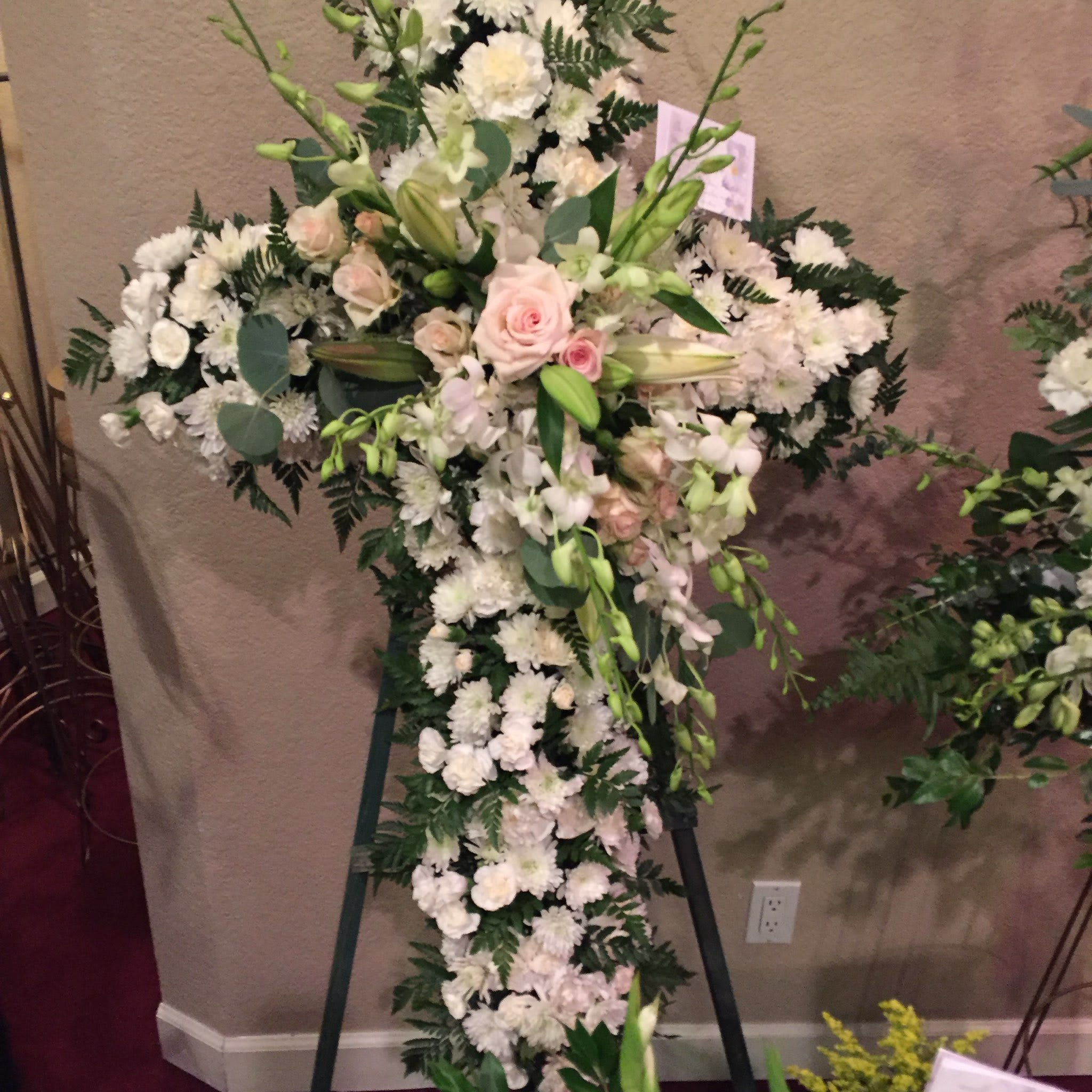 Large white floral cross on an easel with pale pink roses