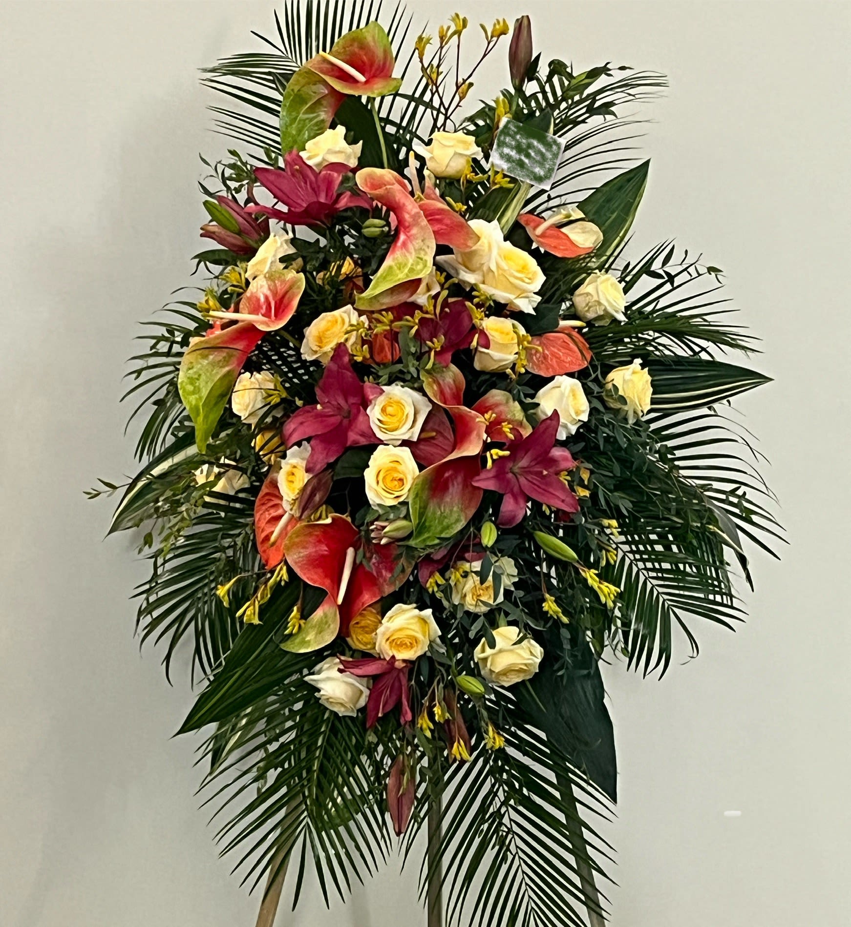 Standing floral spray with roses, anthuriums, and lilies in pink, cream, and red