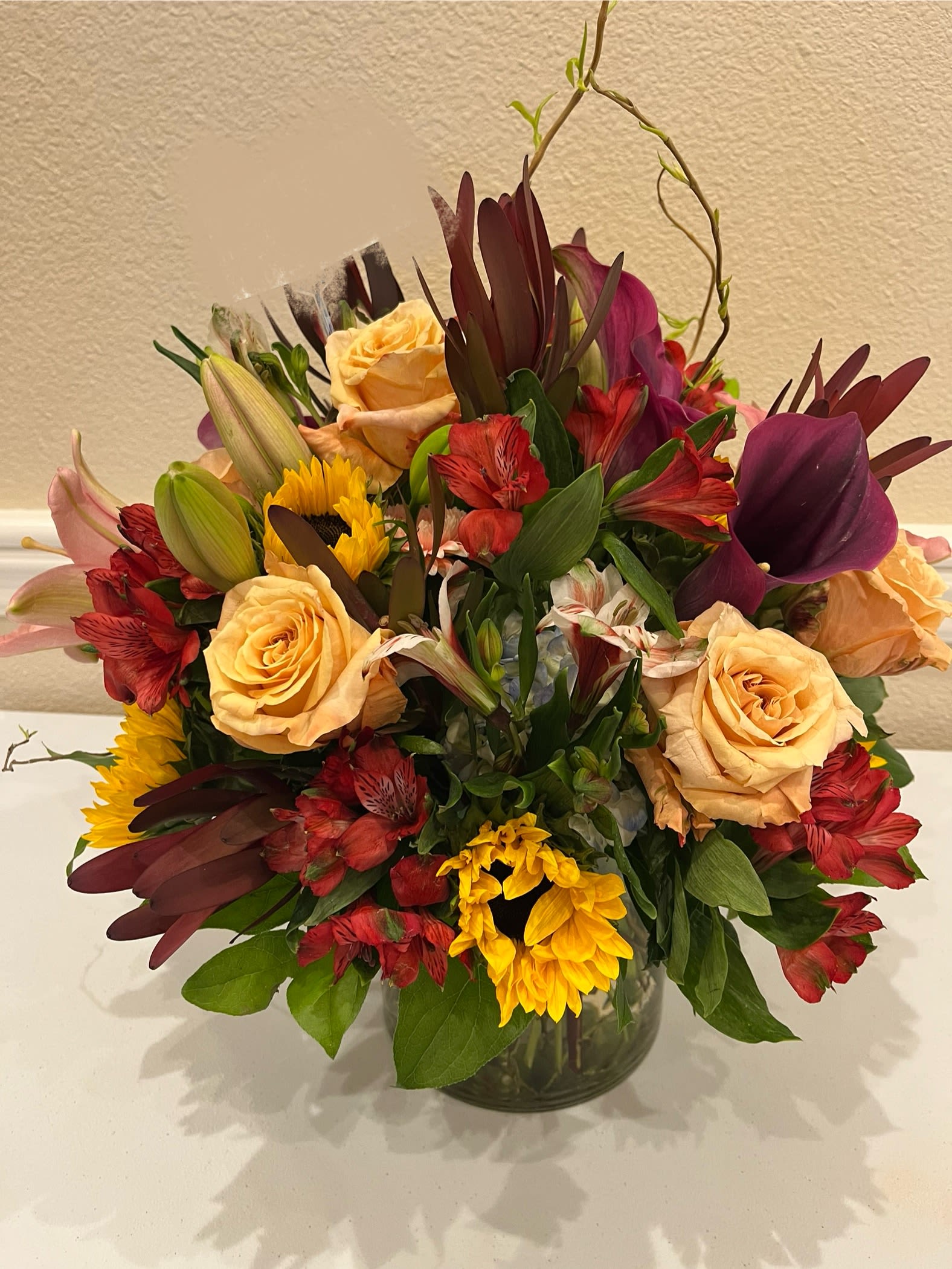 Mixed bouquet of roses, lilies, and sunflowers in a glass vase