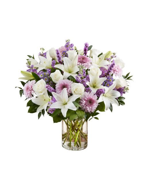 Arrangement of white lilies, white roses, and lavender flowers in a clear glass cylinder vase