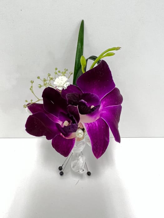 Purple orchid boutonniere with white filler flowers, ribbon, and pins on a white background