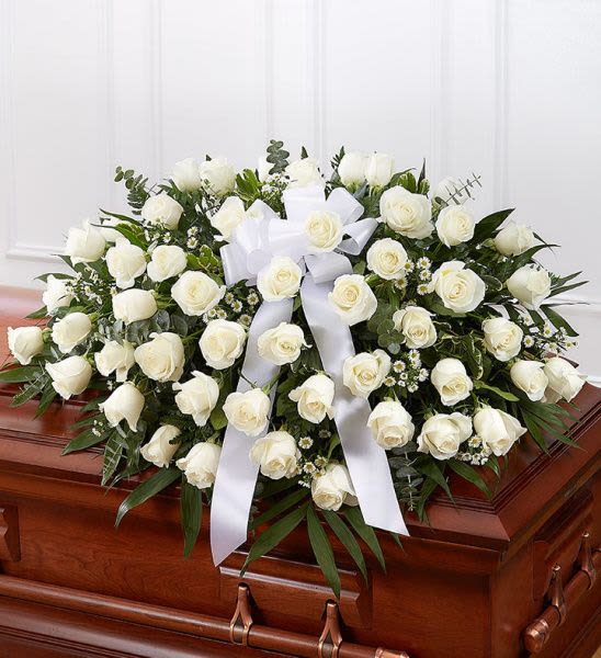 White rose casket spray with large bow on a wooden casket
