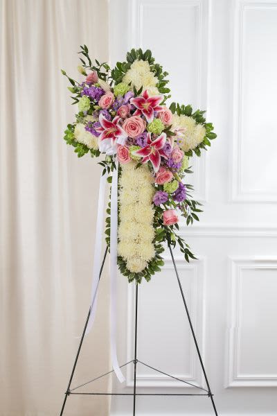 Standing floral cross with white base, pink roses, lilies, and lavender blooms on an easel
