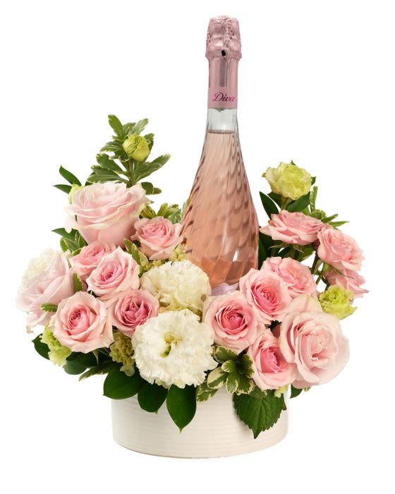 Bottle of pink sparkling wine surrounded by pink roses and white flowers in a white round container