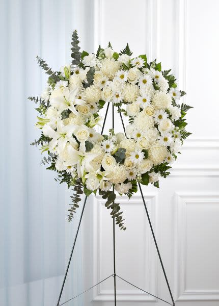 Standing white floral wreath with roses, lilies and mums on a metal easel