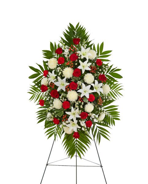 Standing spray of red roses, white lilies, and white mums with large palm fronds on an easel