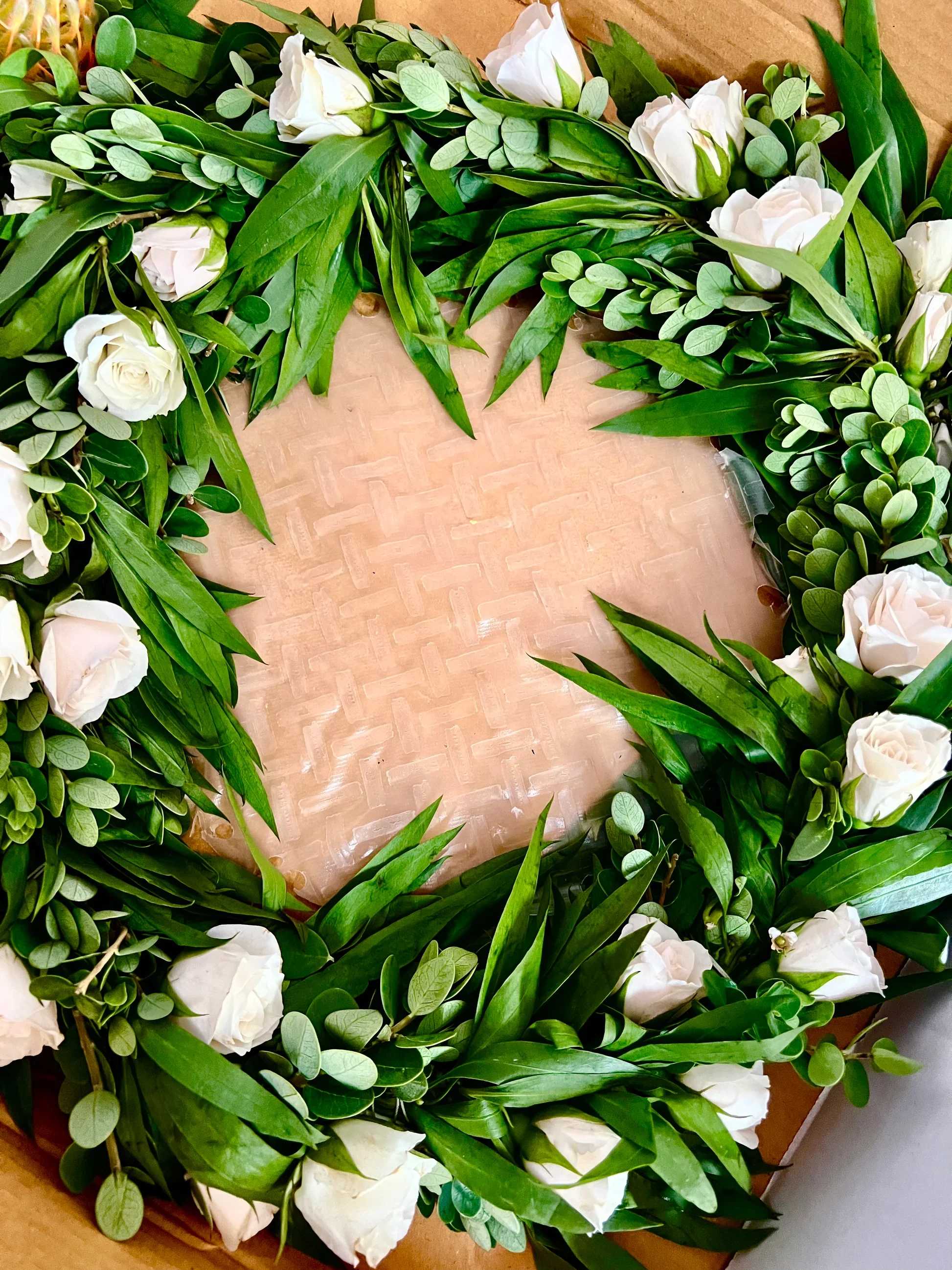 Wreath of white roses and greenery arranged in a circle on a flat base