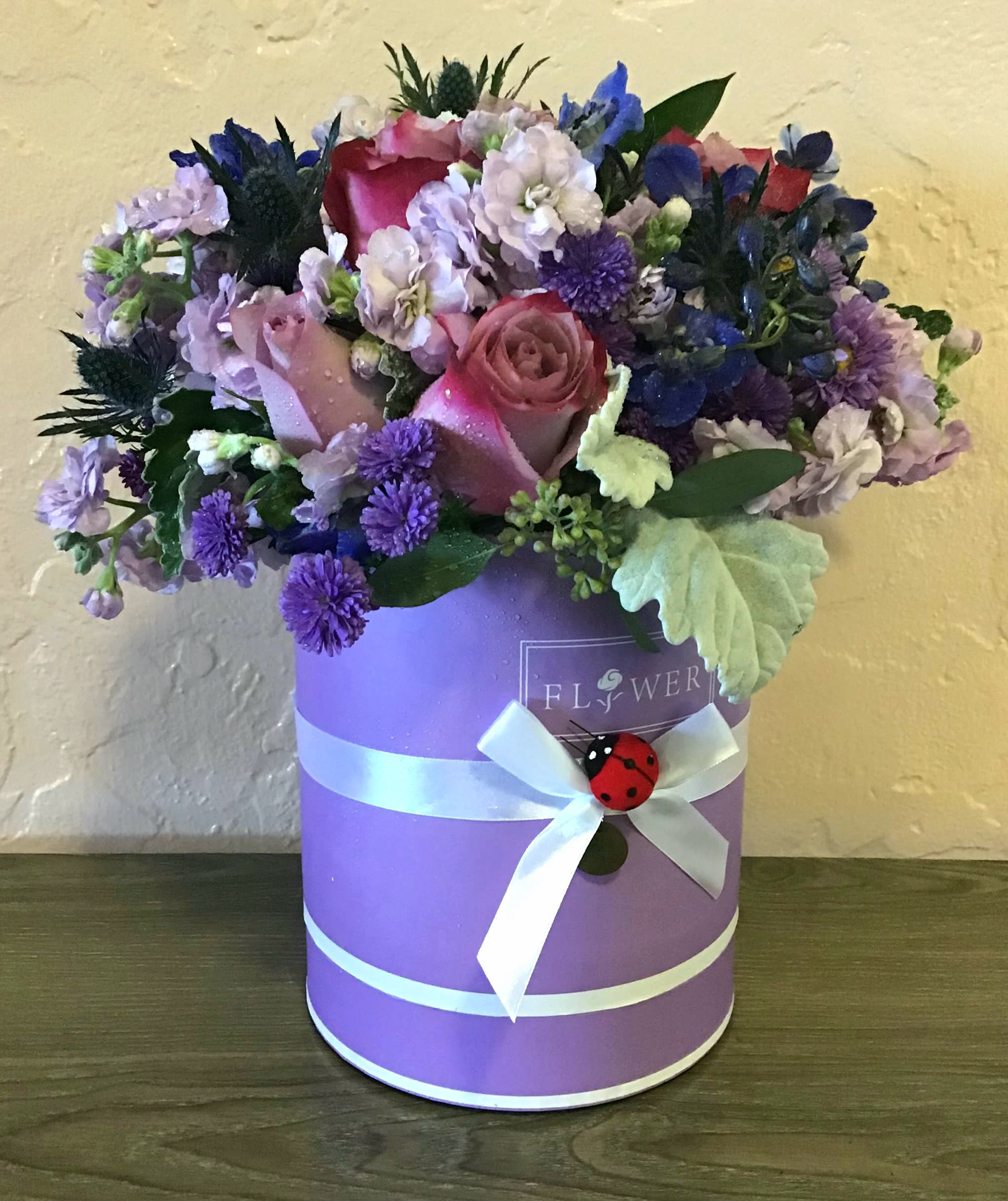 Pink and purple flower arrangement in a lavender hat box with a white ribbon