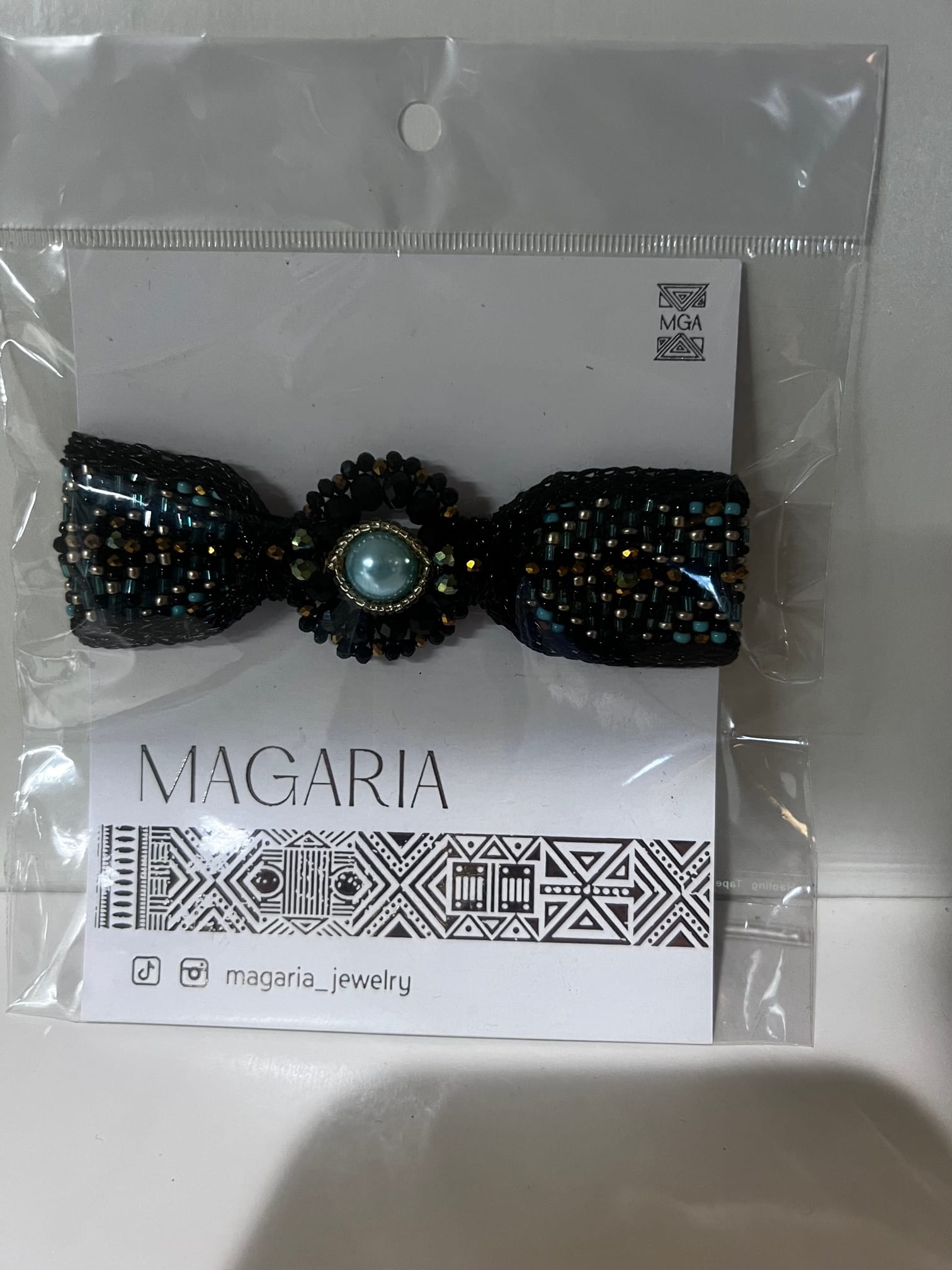 Beaded black bow hair accessory in plastic packaging
